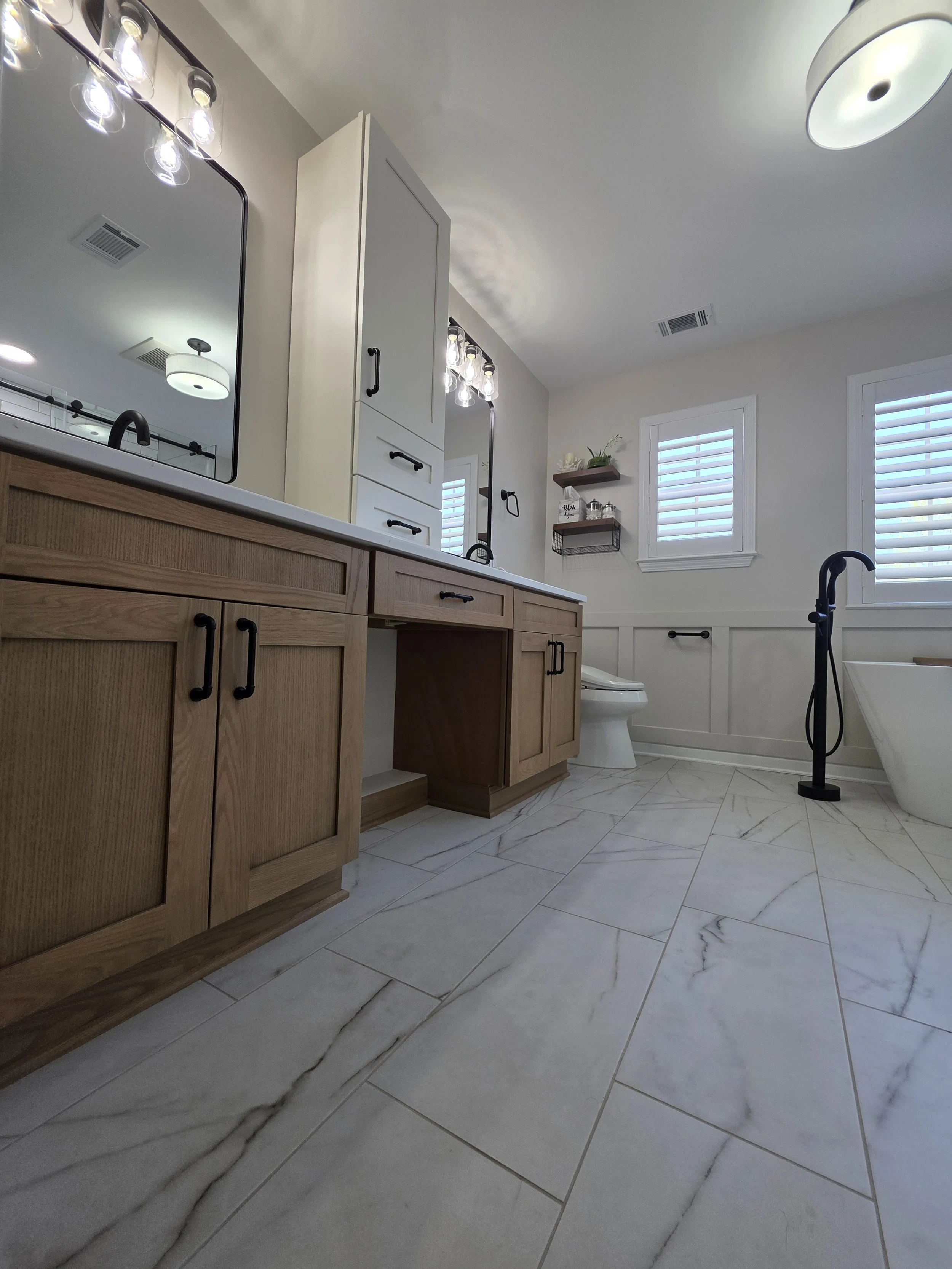 Low view along the wood-tone vanity cabinetry and marble-look floor toward the shuttered bathroom windows.