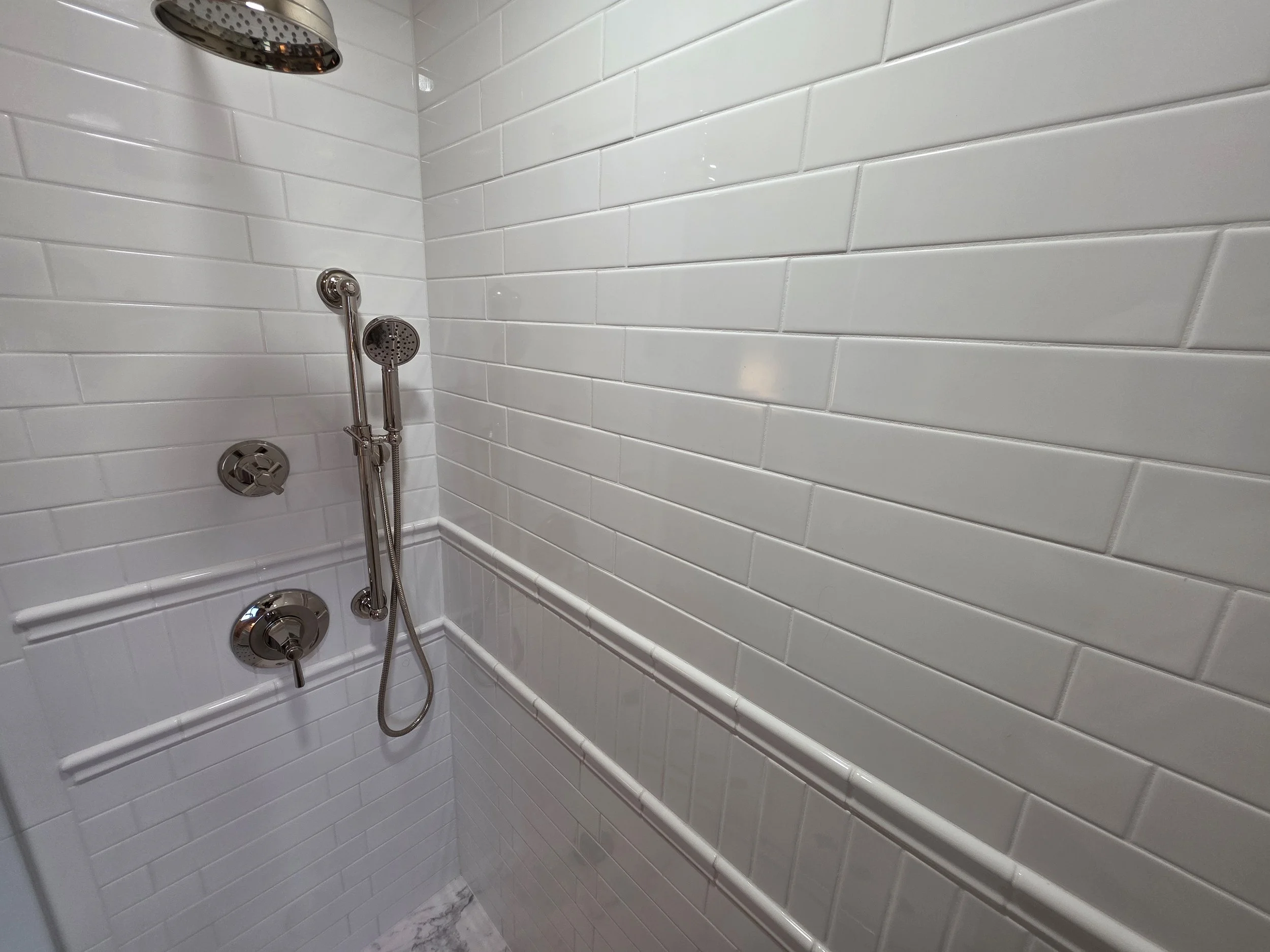 Handheld shower fixture against white subway tile.