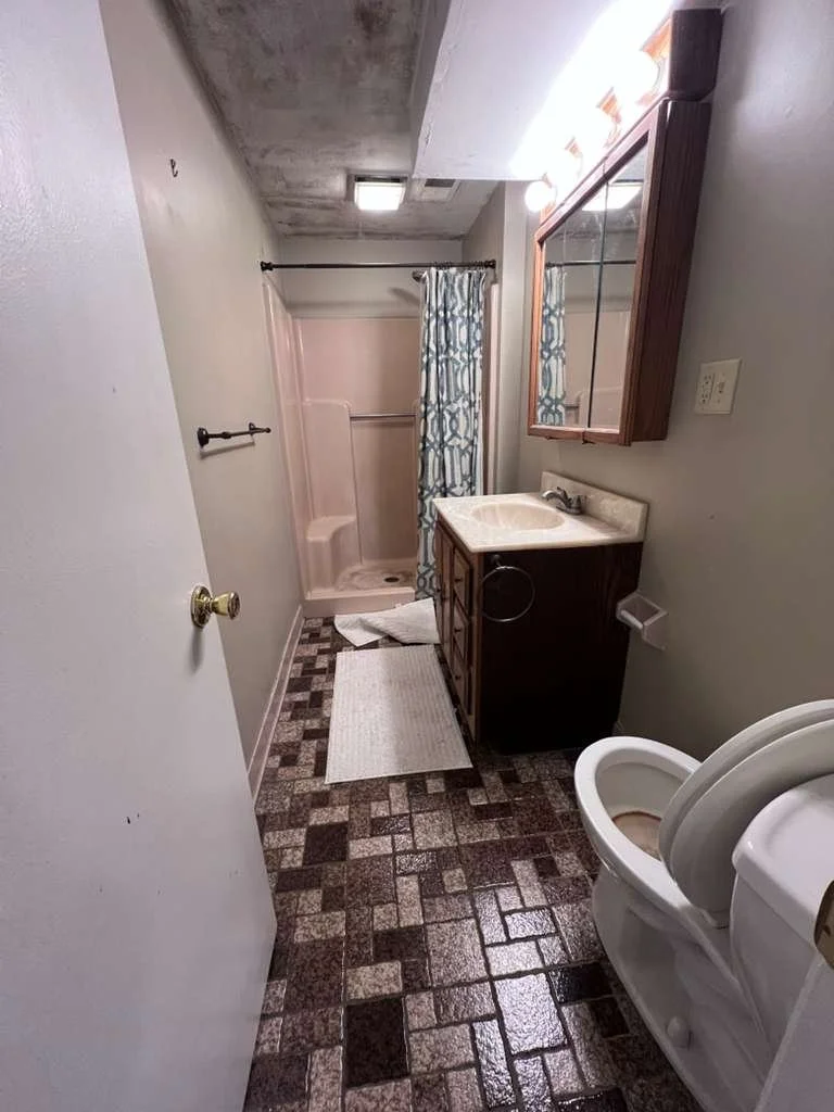 Before renovation: view along the original vanity toward the curtained tub and older ceiling.