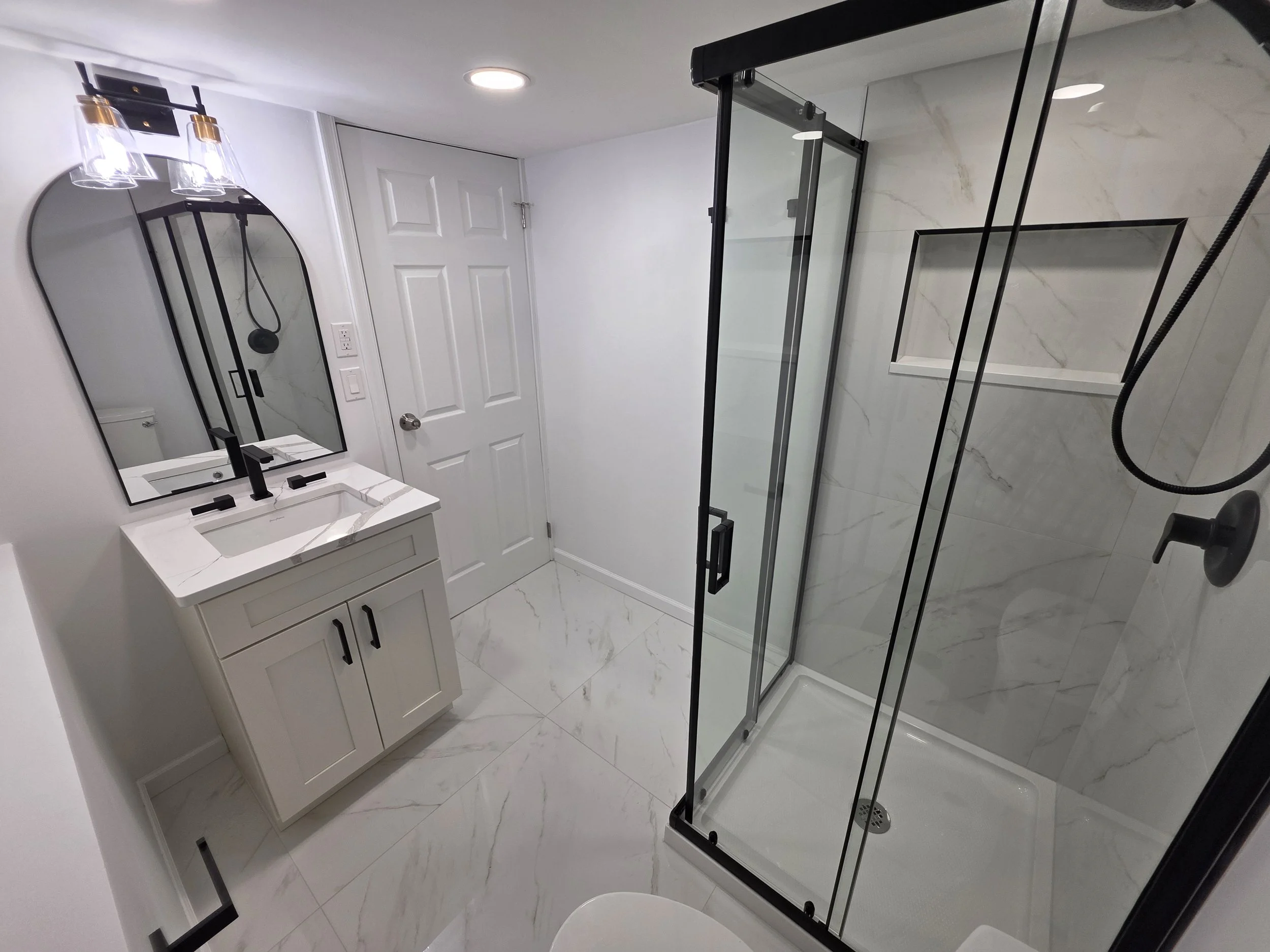 Samuel’s remodeled basement bathroom with a black-framed corner shower, white vanity and marble-look tile.