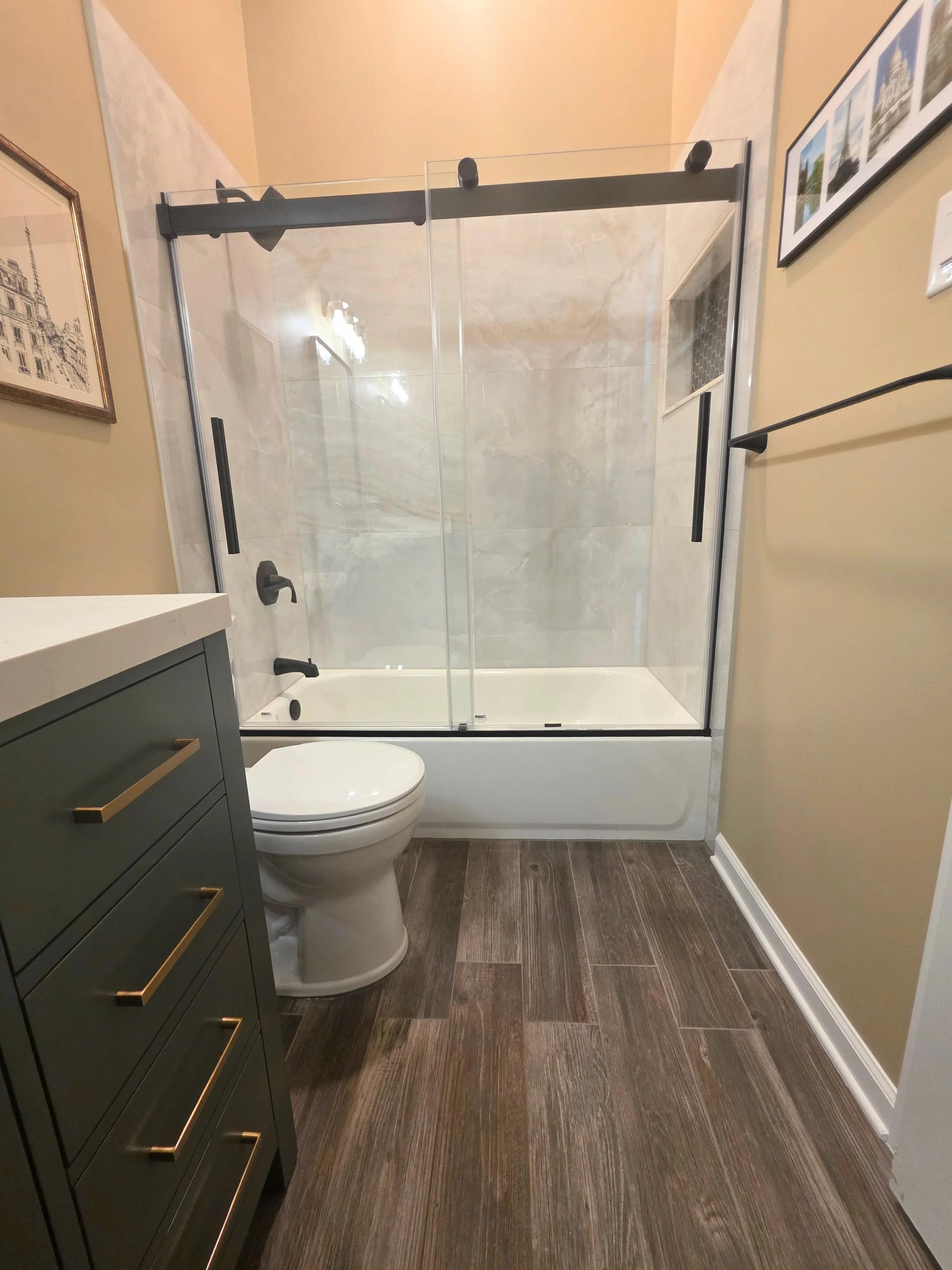 View toward the bathtub and glass enclosure beside the green vanity and toilet.