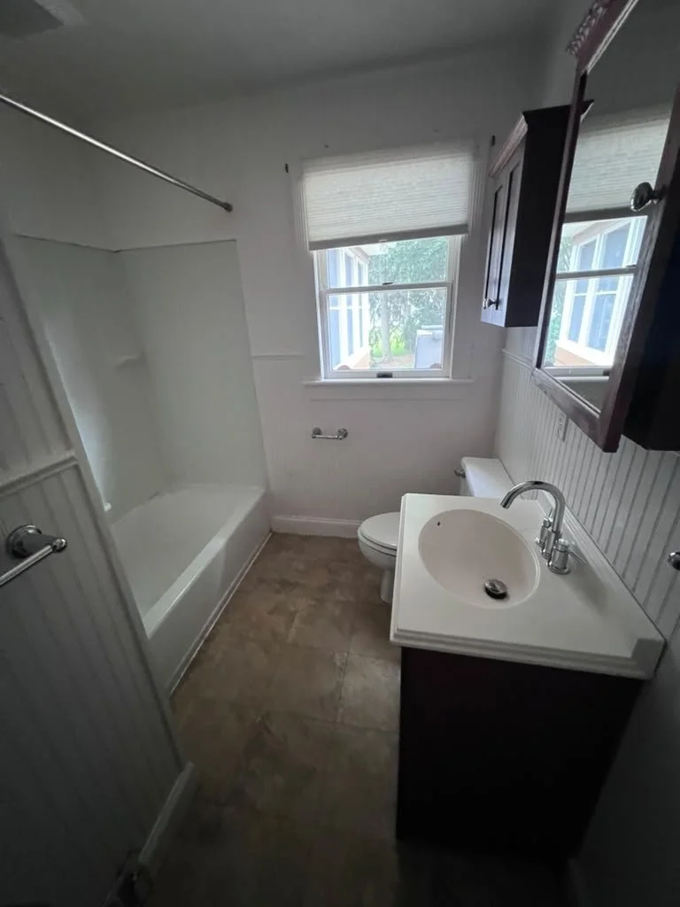 Hallway bathroom before renovation with tub and pedestal-style sink.