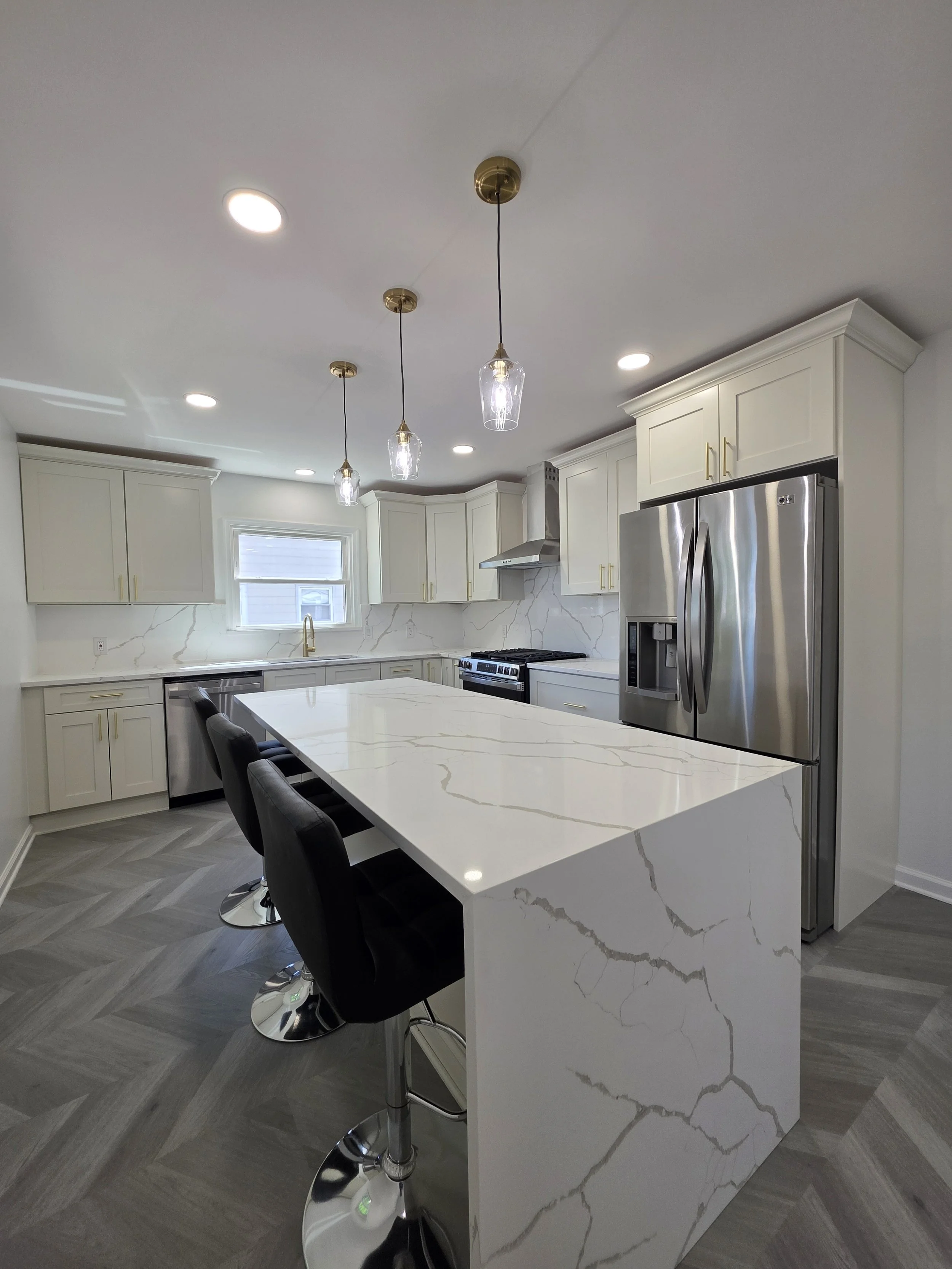 View down the waterfall island toward the sink and stainless refrigerator.