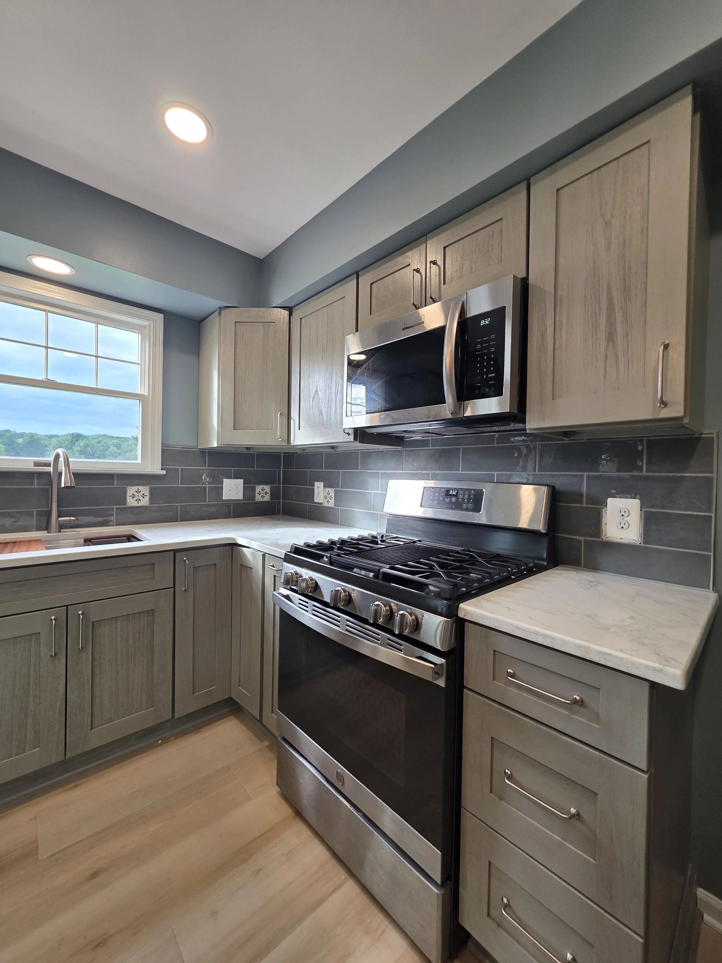 Stainless steel range and microwave with gray cabinets.