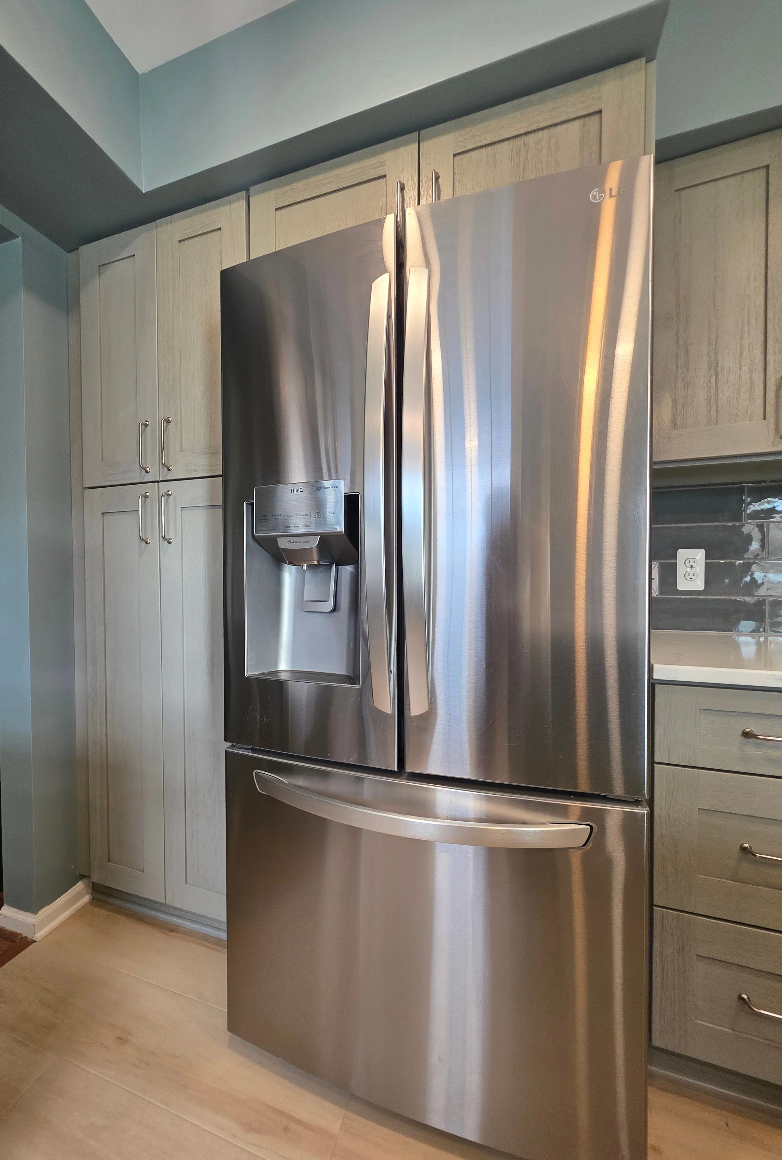Stainless steel refrigerator surrounded by gray cabinets.