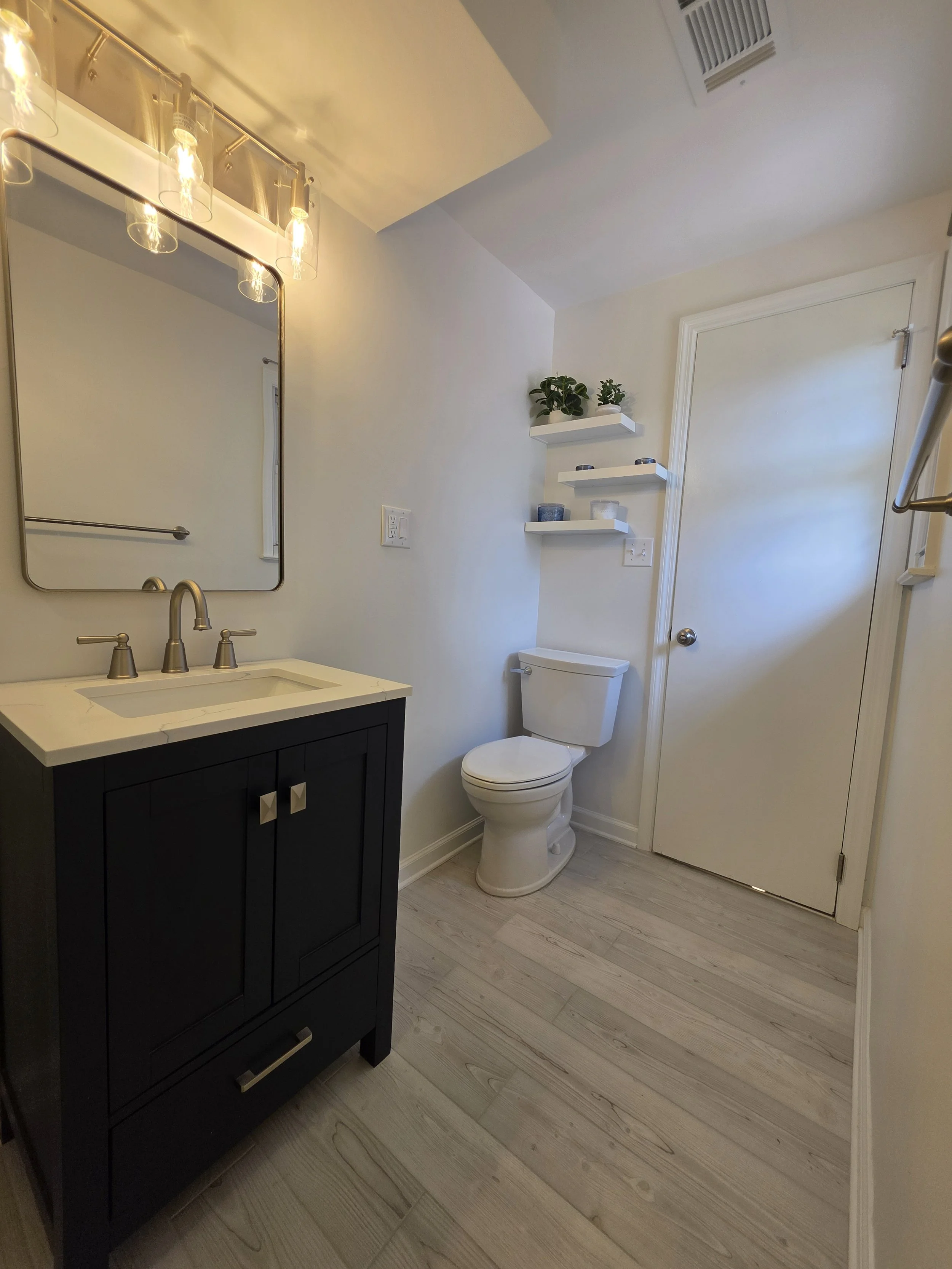 Navy vanity and toilet with wall shelves near the bathroom doorway.