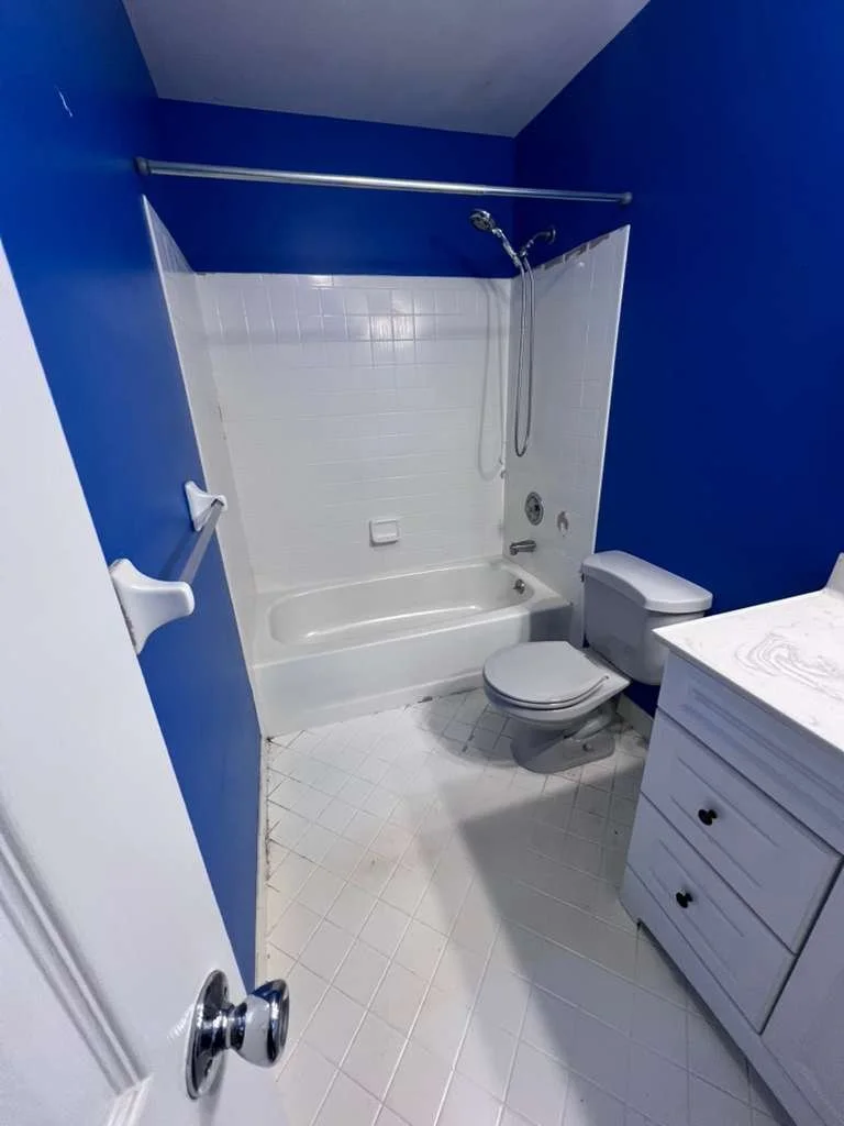 Before renovation: the original hallway bathroom with blue walls, a white tub surround and a gray vanity.