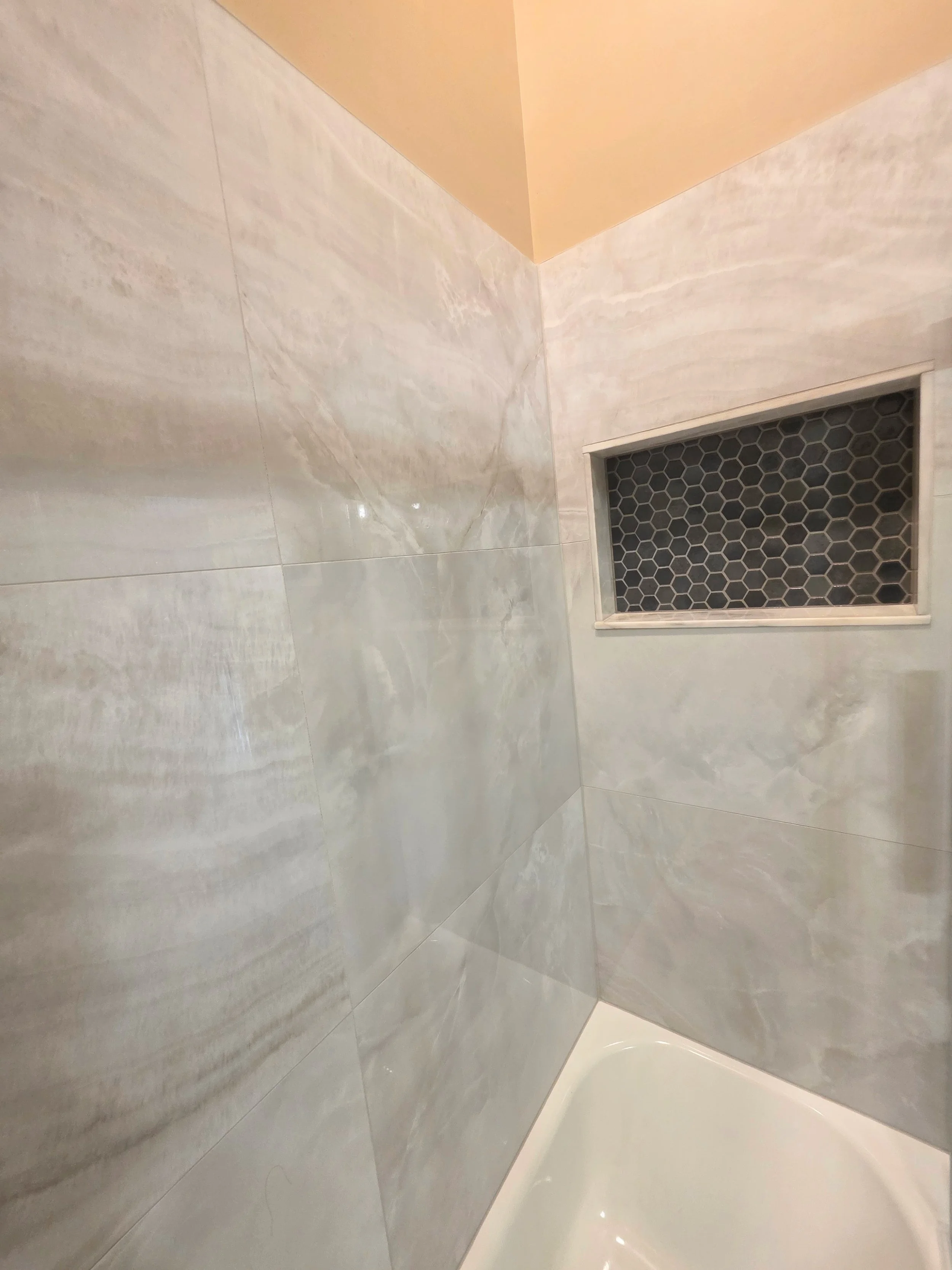 White bathtub beside light wall tile and a dark hexagonal-tile recessed niche.