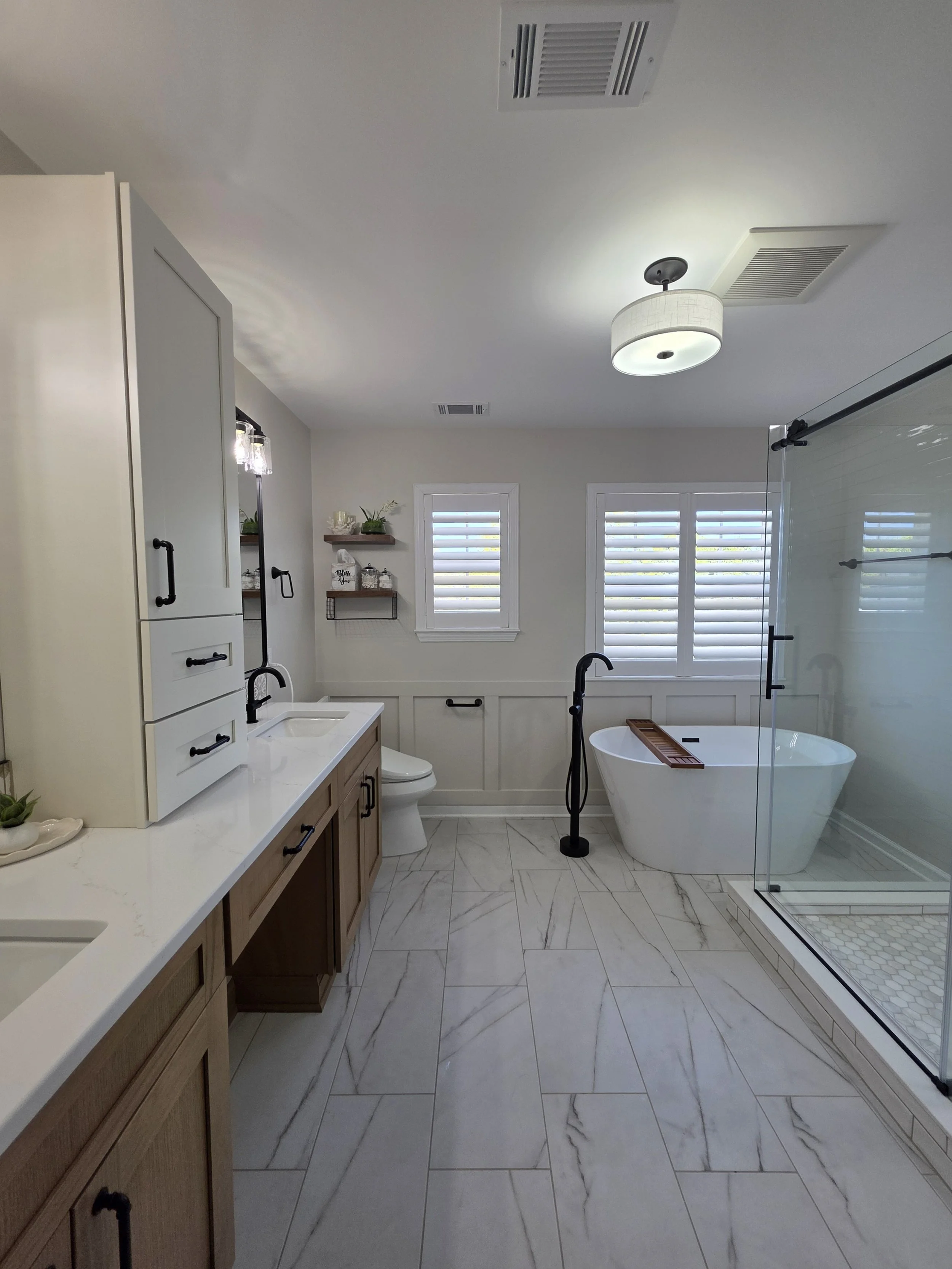 Finished master bathroom with a wood-tone double vanity, freestanding tub, glass shower and a neutral tile palette.