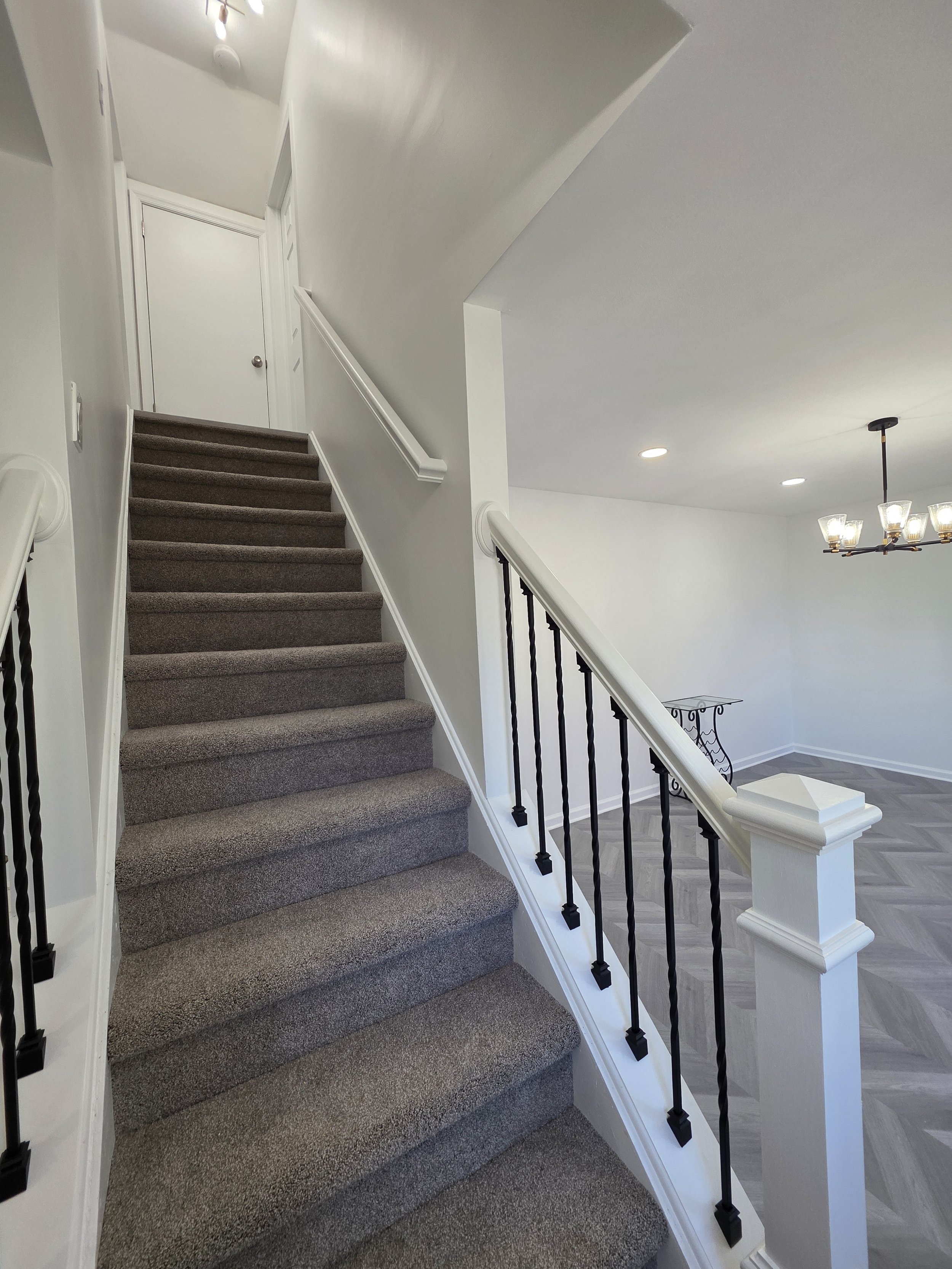 Remodeled staircase with white rails and posts, dark balusters and carpeted treads.