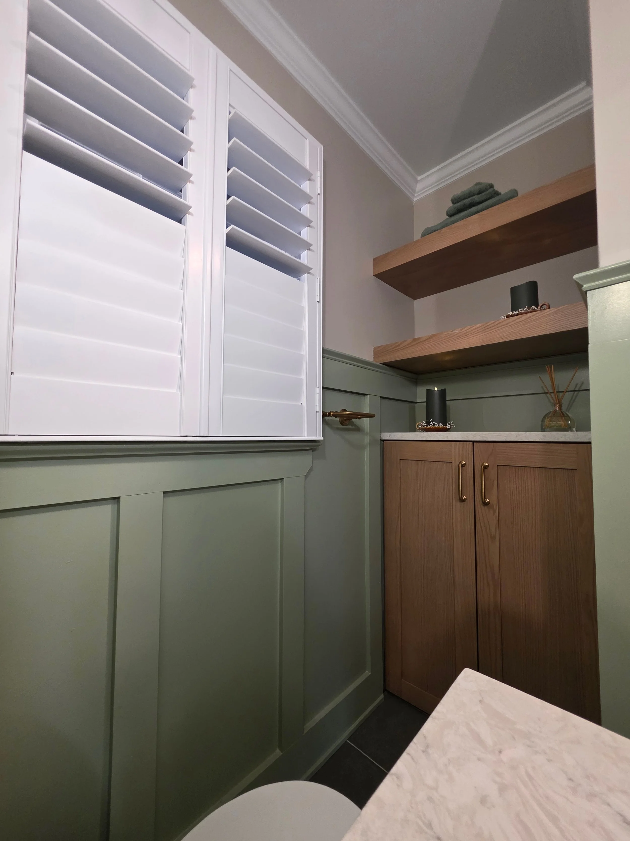 Window shutters and green paneling beside wood vanity.