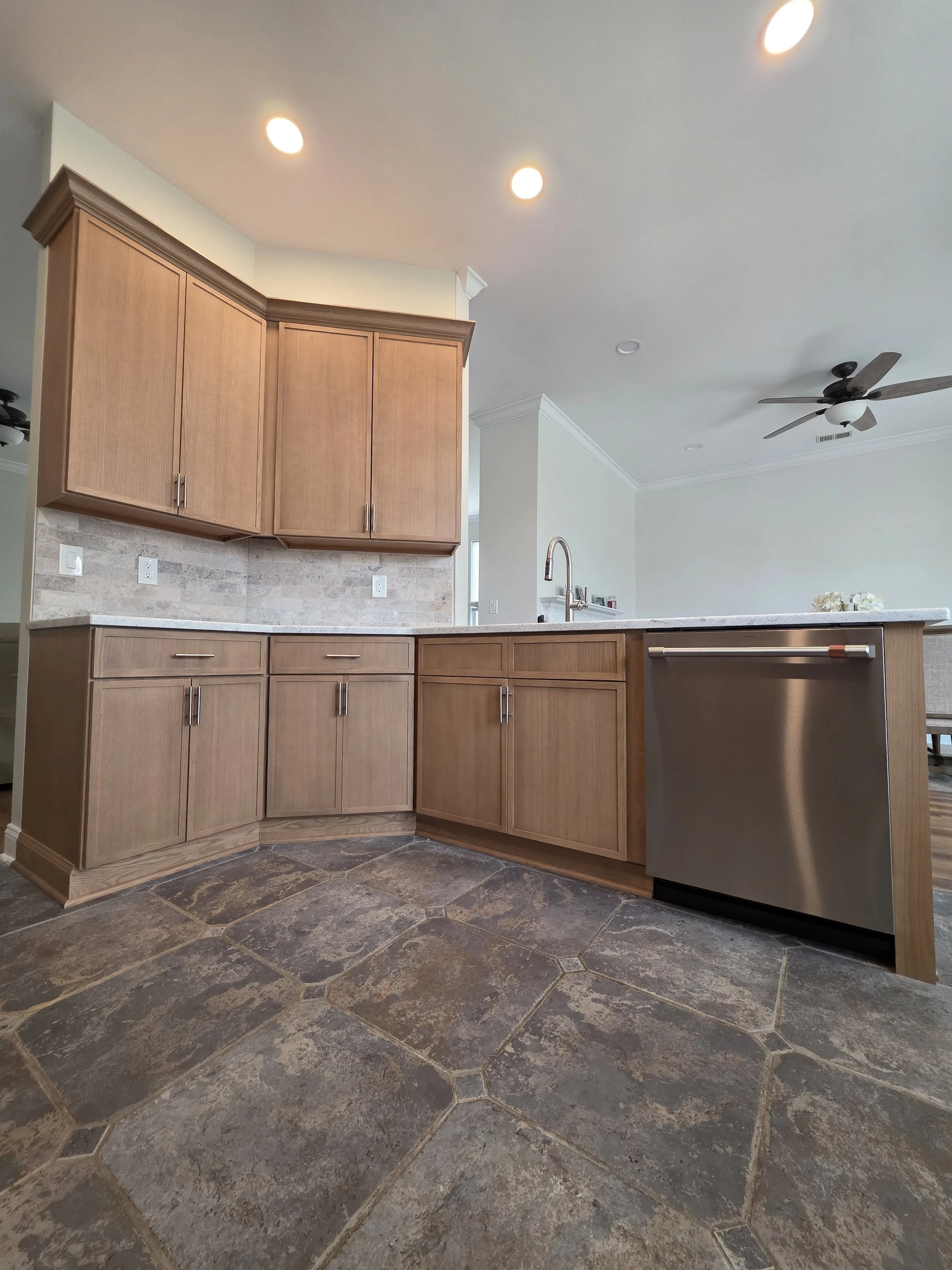 Corner wood cabinetry beside the dishwasher and peninsula, with patterned floor tile.