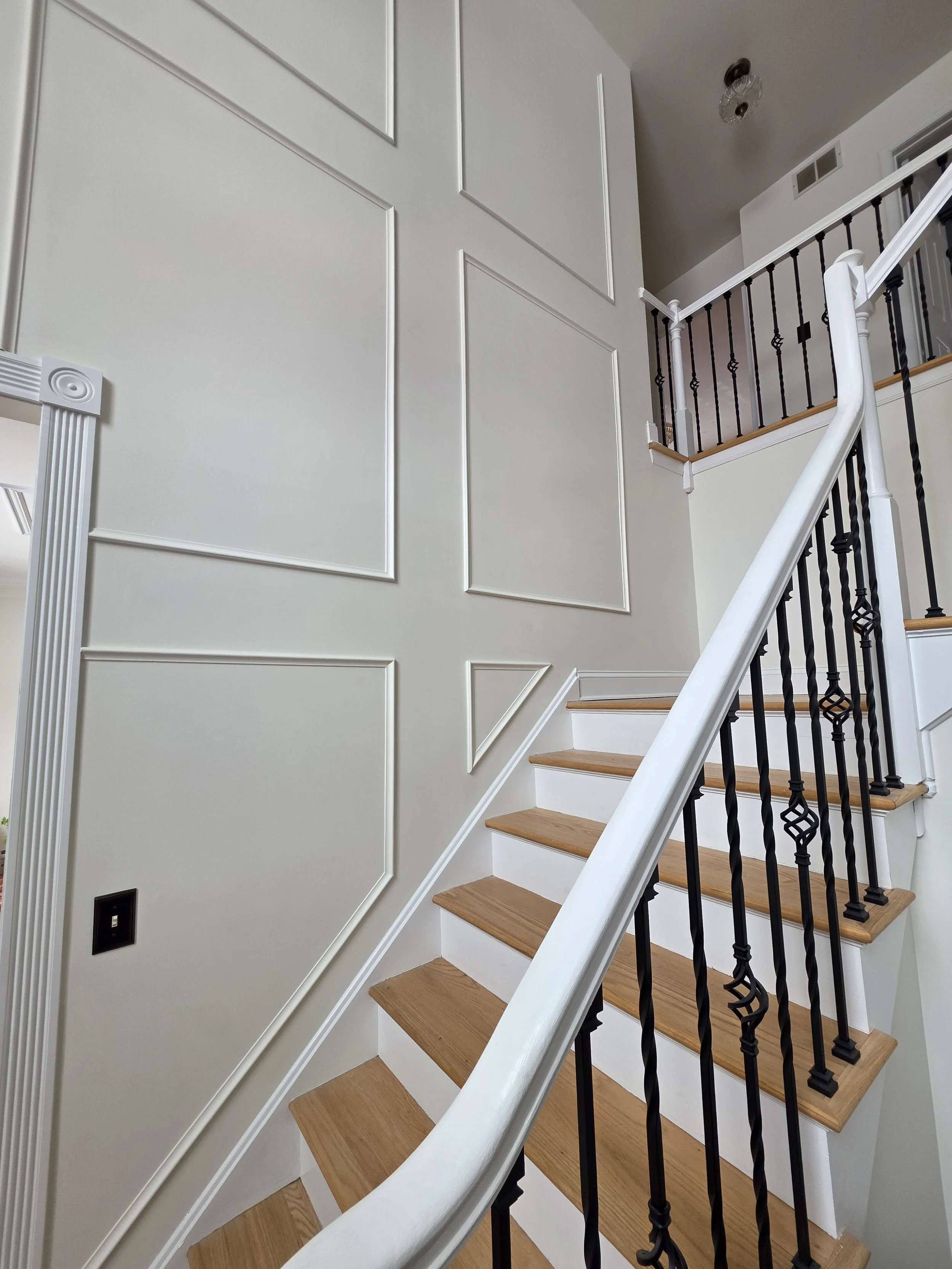 Close view of the staircase beside tall rectangular wall trim and a white handrail.