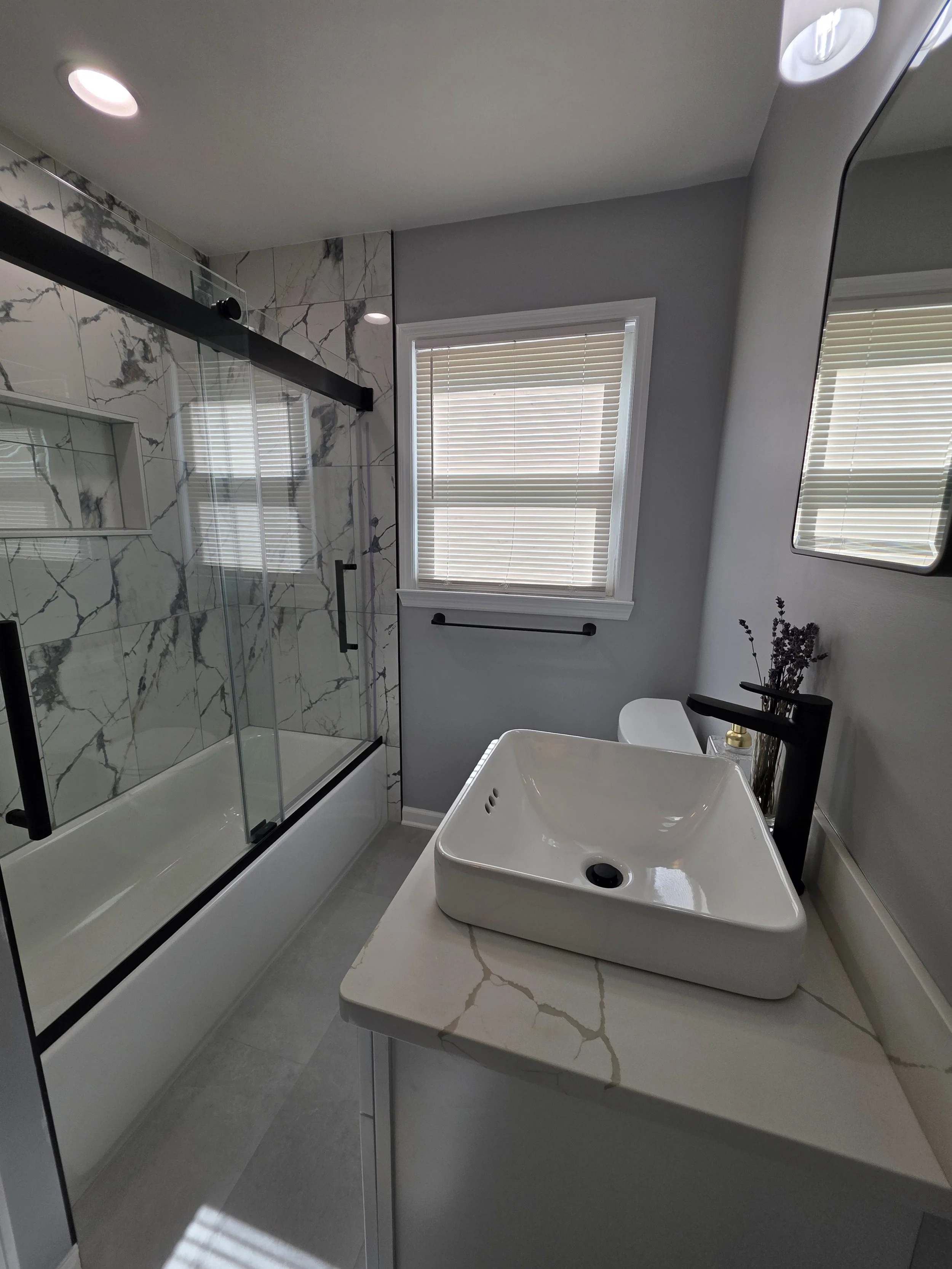 Angela’s remodeled hallway bathroom with a white vessel-sink vanity, glass tub enclosure and striking veined wall tile.