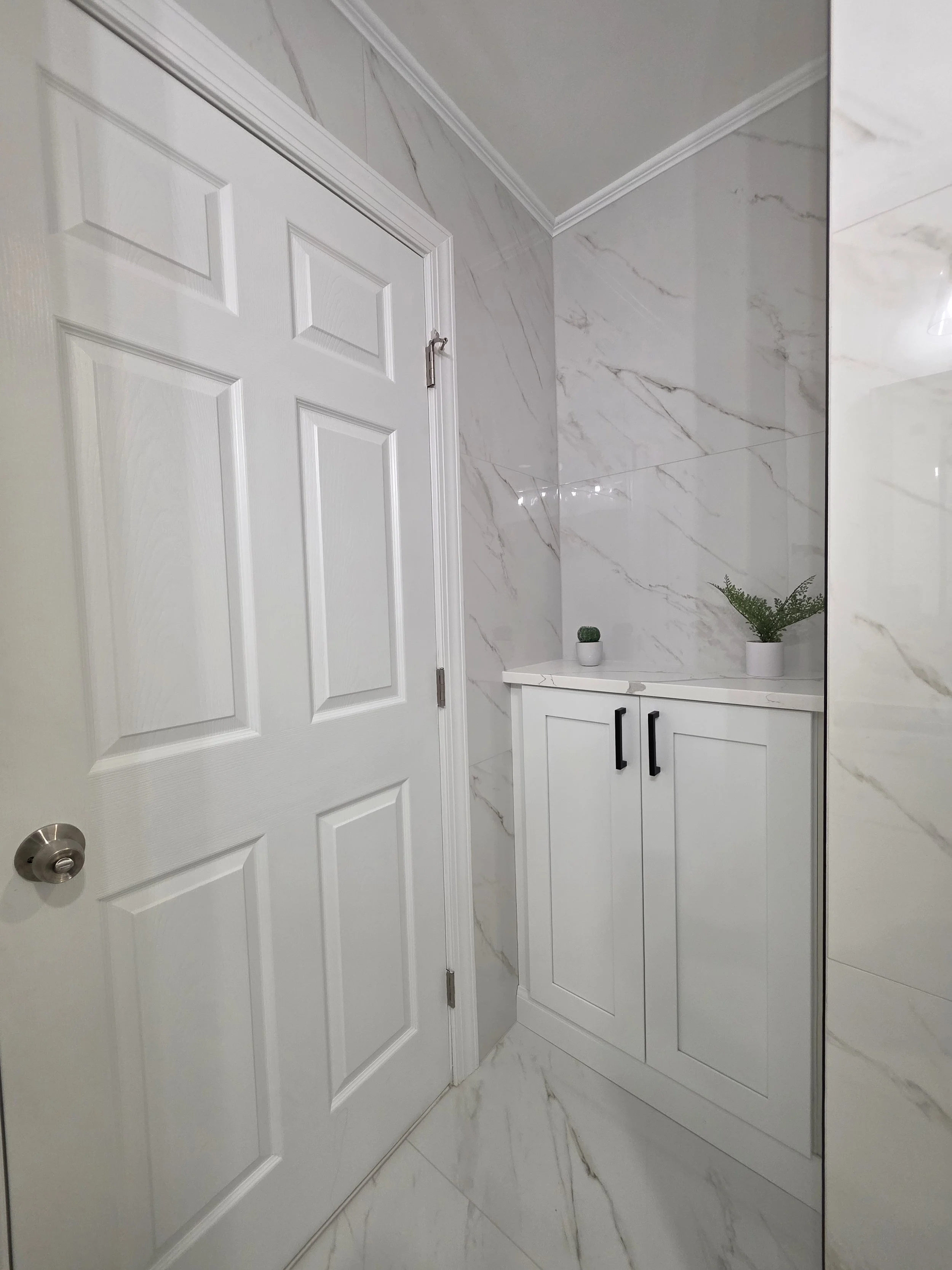 Bathroom doorway beside the gray vanity and marble-look tiled wall, with black cabinet pulls.