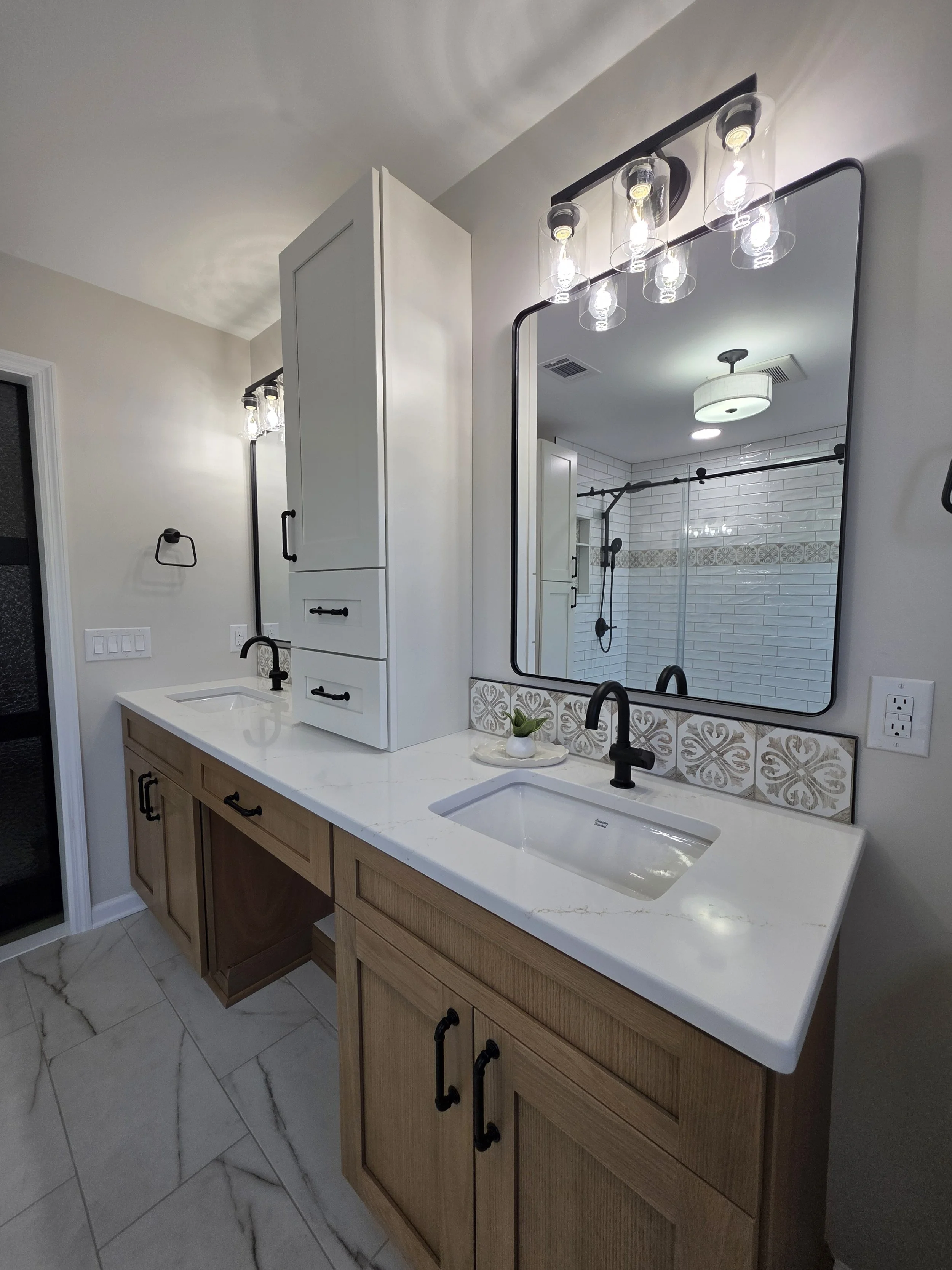 Double vanity with white sinks, black faucets, rectangular mirrors and a tall white storage cabinet.