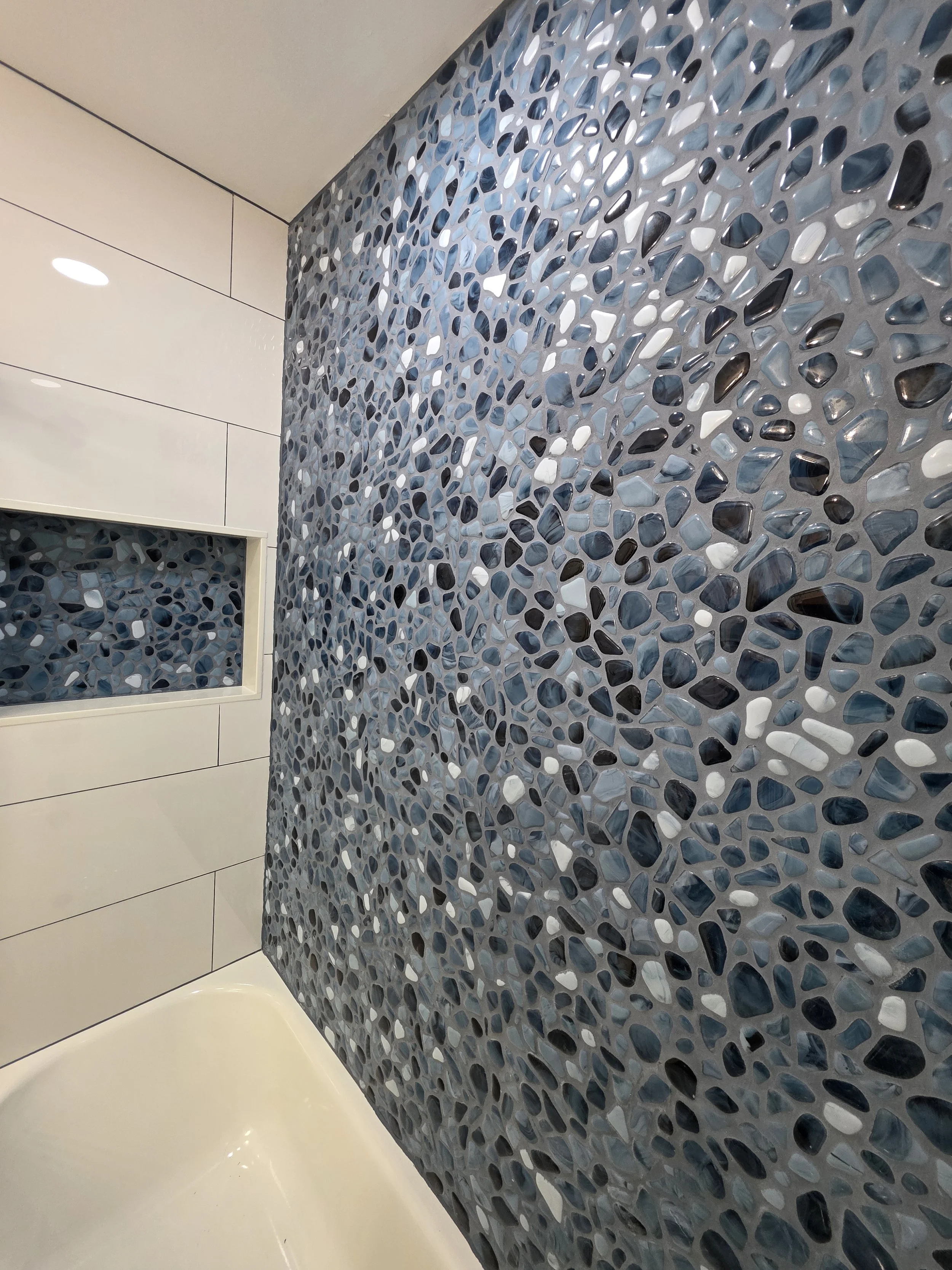 Close view of the blue accent wall and recessed niche beside the white bathtub.