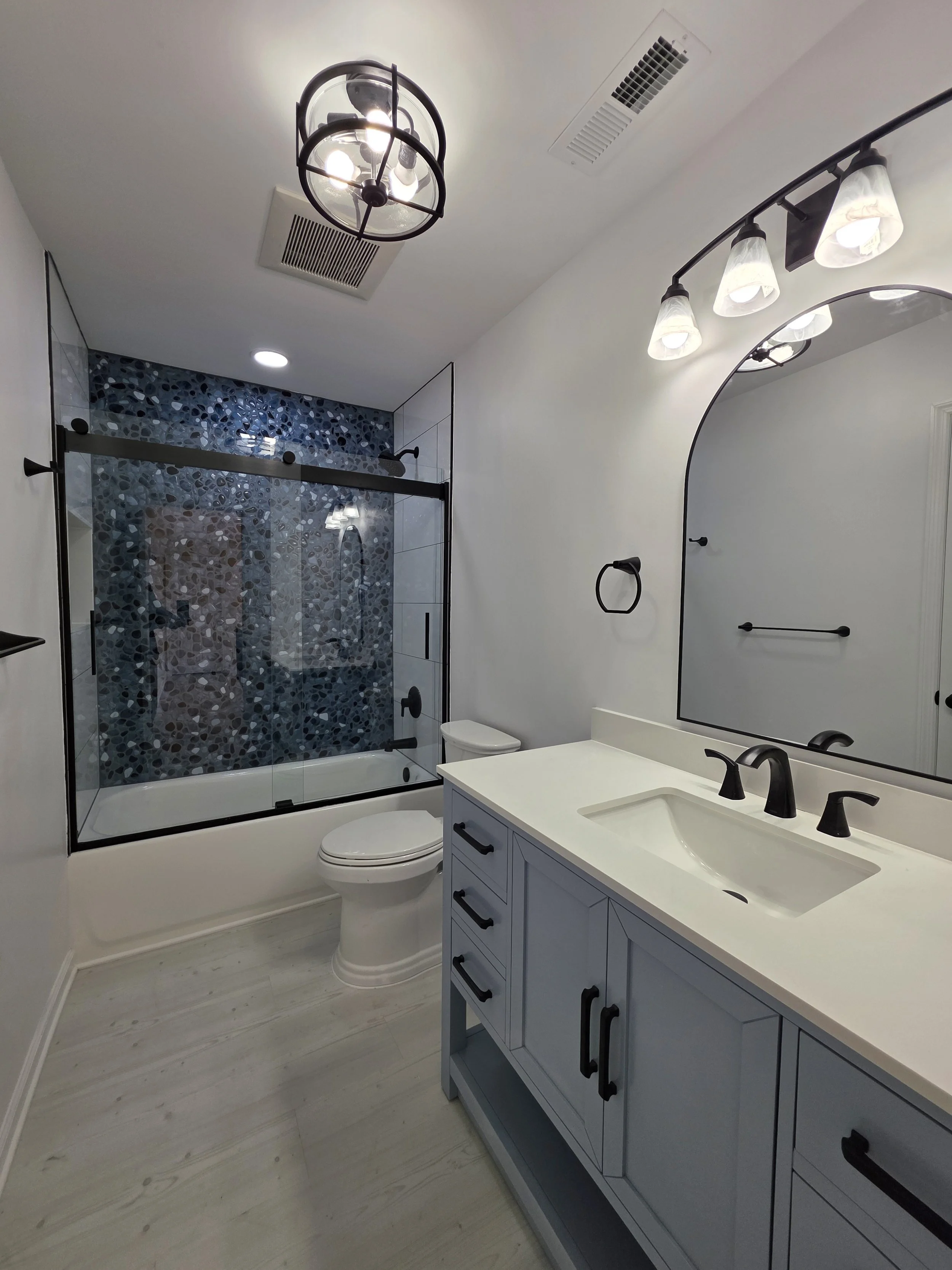 View along the gray vanity toward the glass tub enclosure and blue tile accent wall.