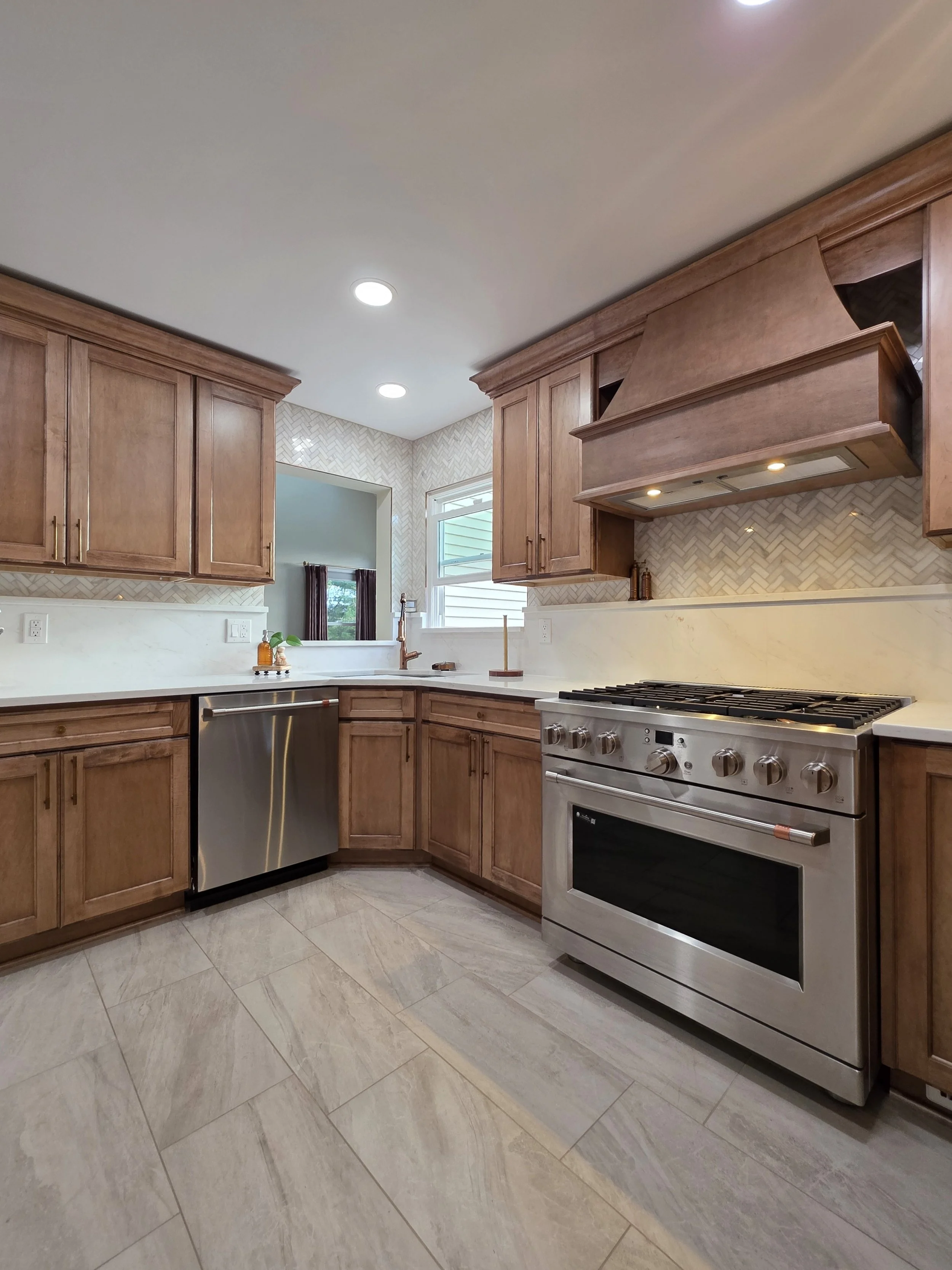 Stainless range and matching wood hood beside the sink, dishwasher and light backsplash.