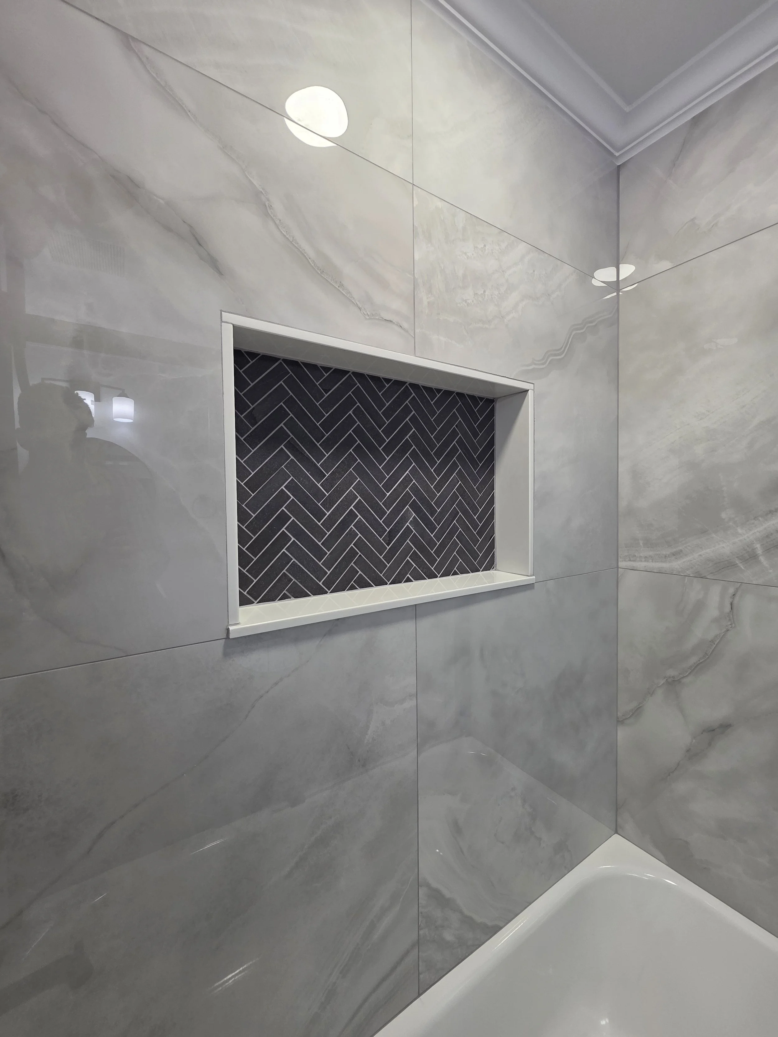 Angled view of the wide shower niche, marble-look wall tile and white tub edge.