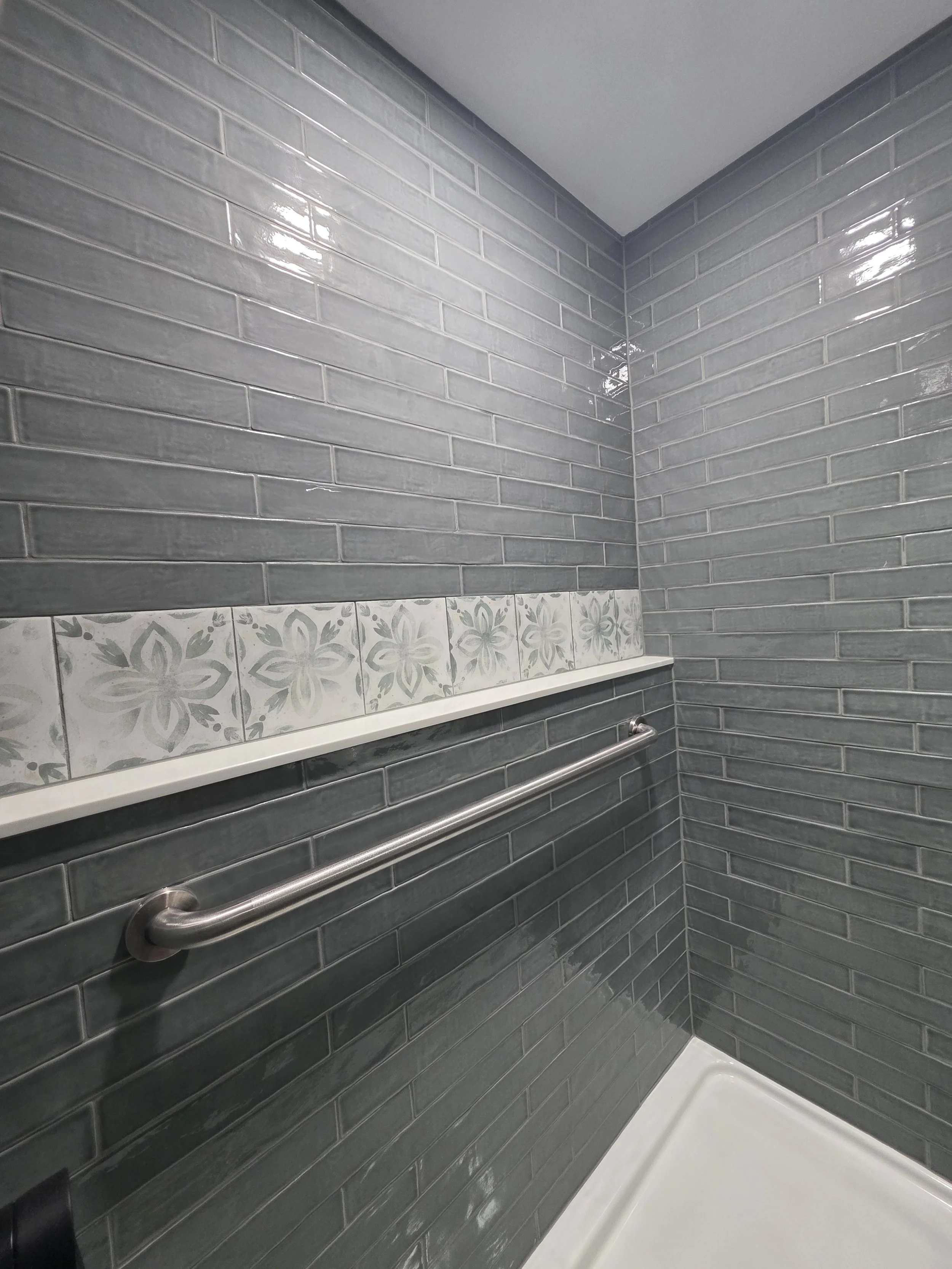 Shower corner with gray subway-style tile and the decorative ledge.