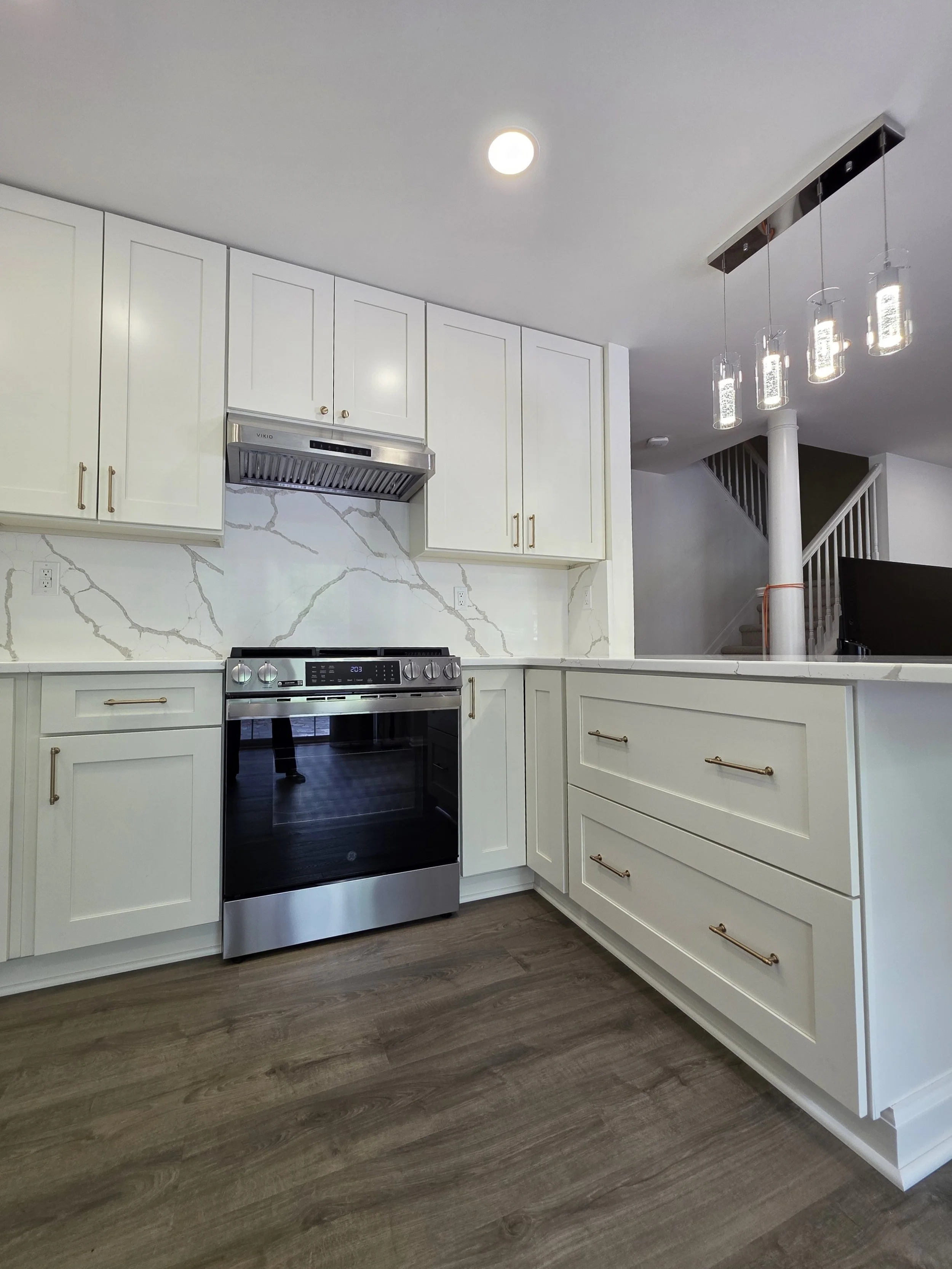 Stainless range and white drawers beside the peninsula with matching veined surfaces.