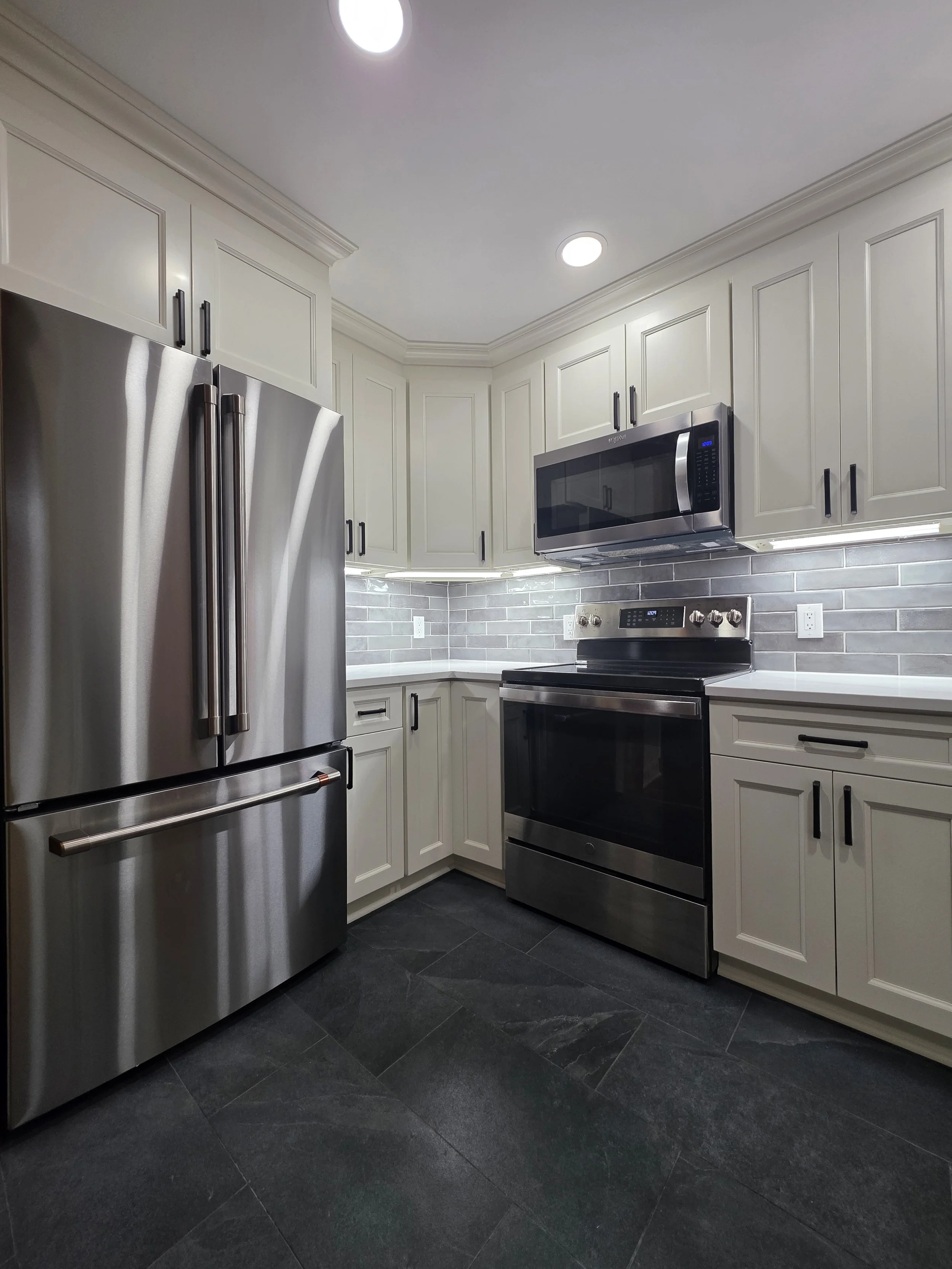 Stainless refrigerator and range beneath light cabinetry and recessed lights.