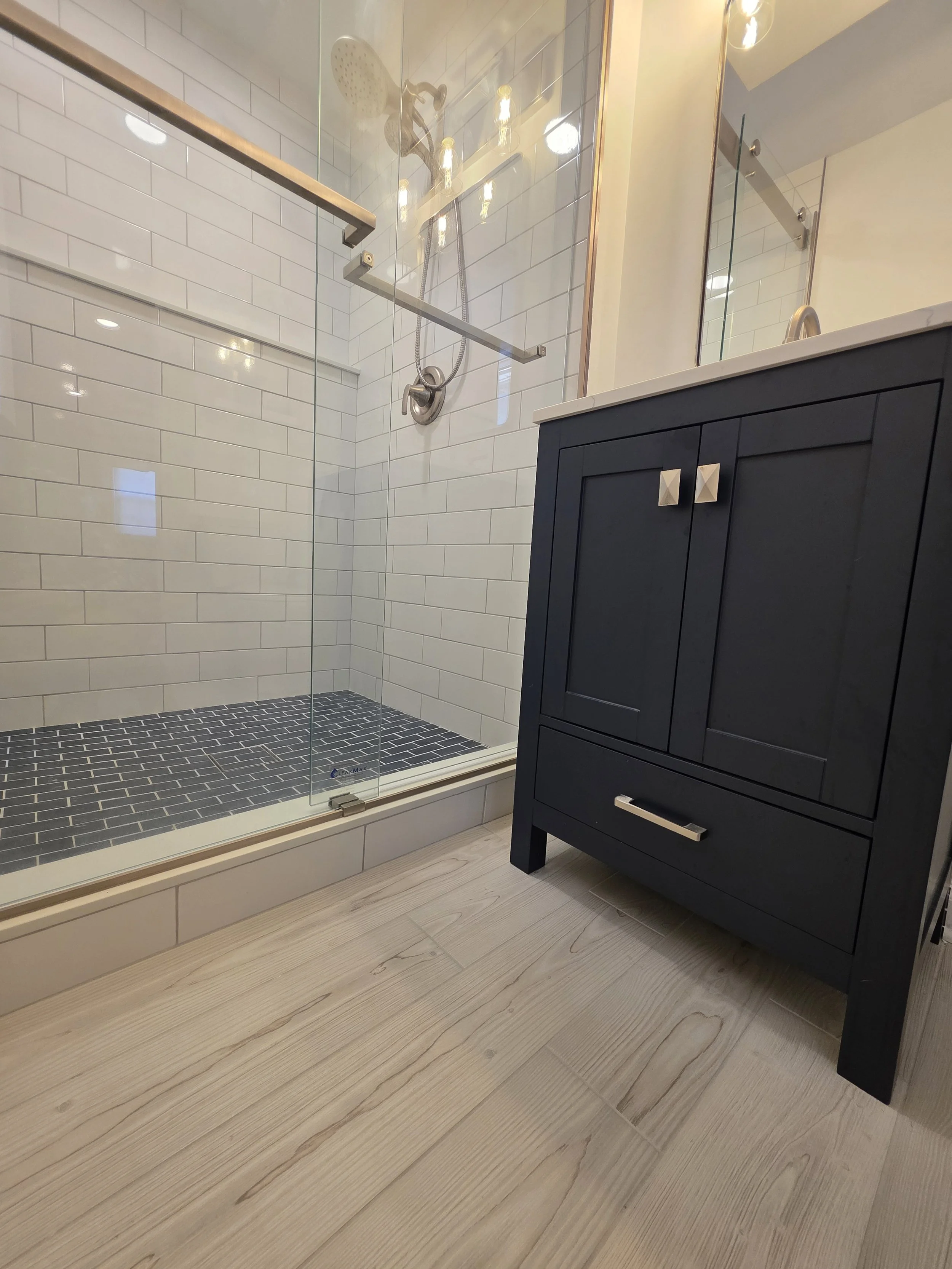 Katie and Mike’s remodeled basement bathroom with a navy vanity, glass shower and white subway tile.