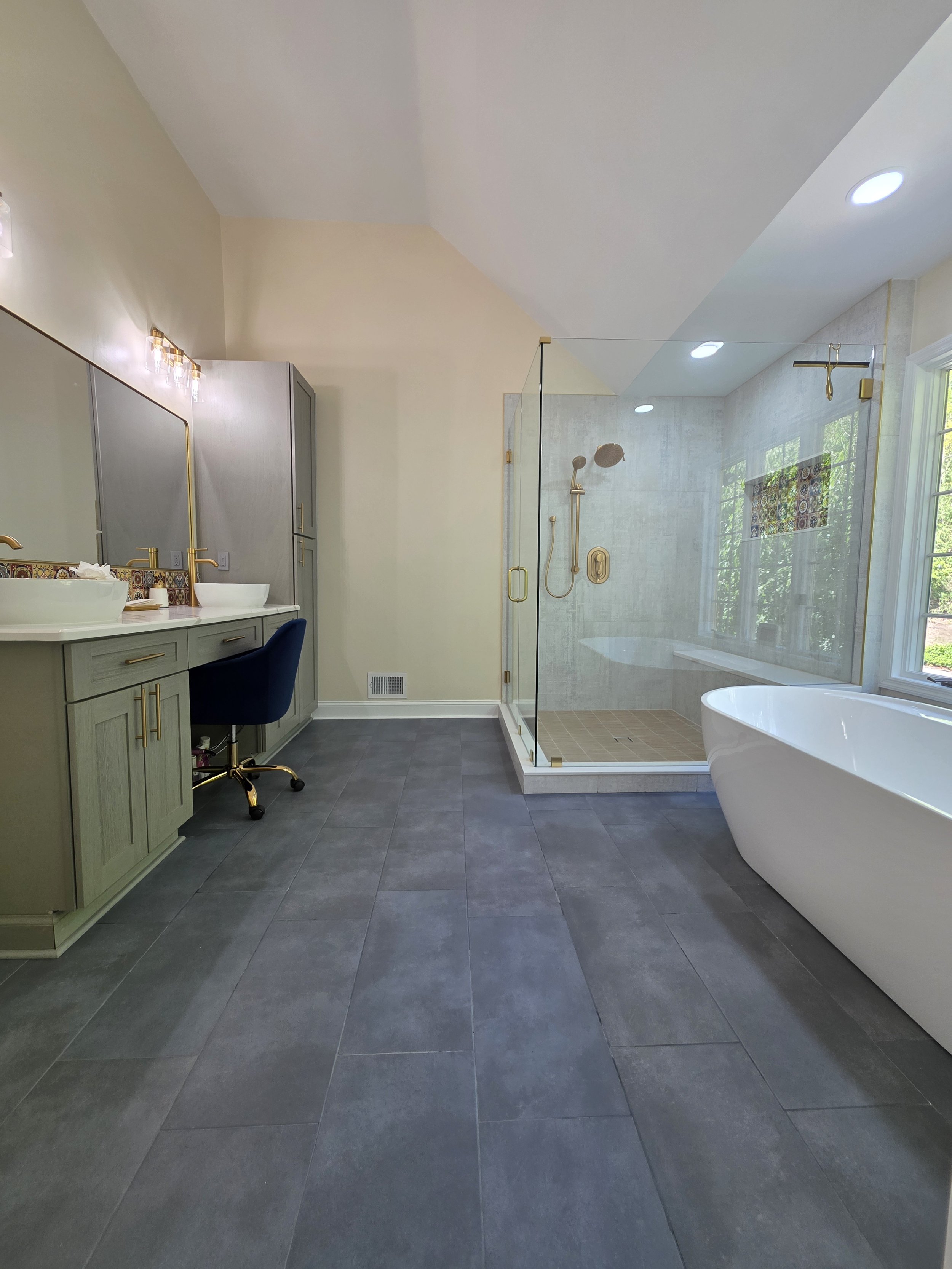 Wide view of the remodeled master bathroom with woodgrain vanity, glass shower, freestanding tub and dark floor.