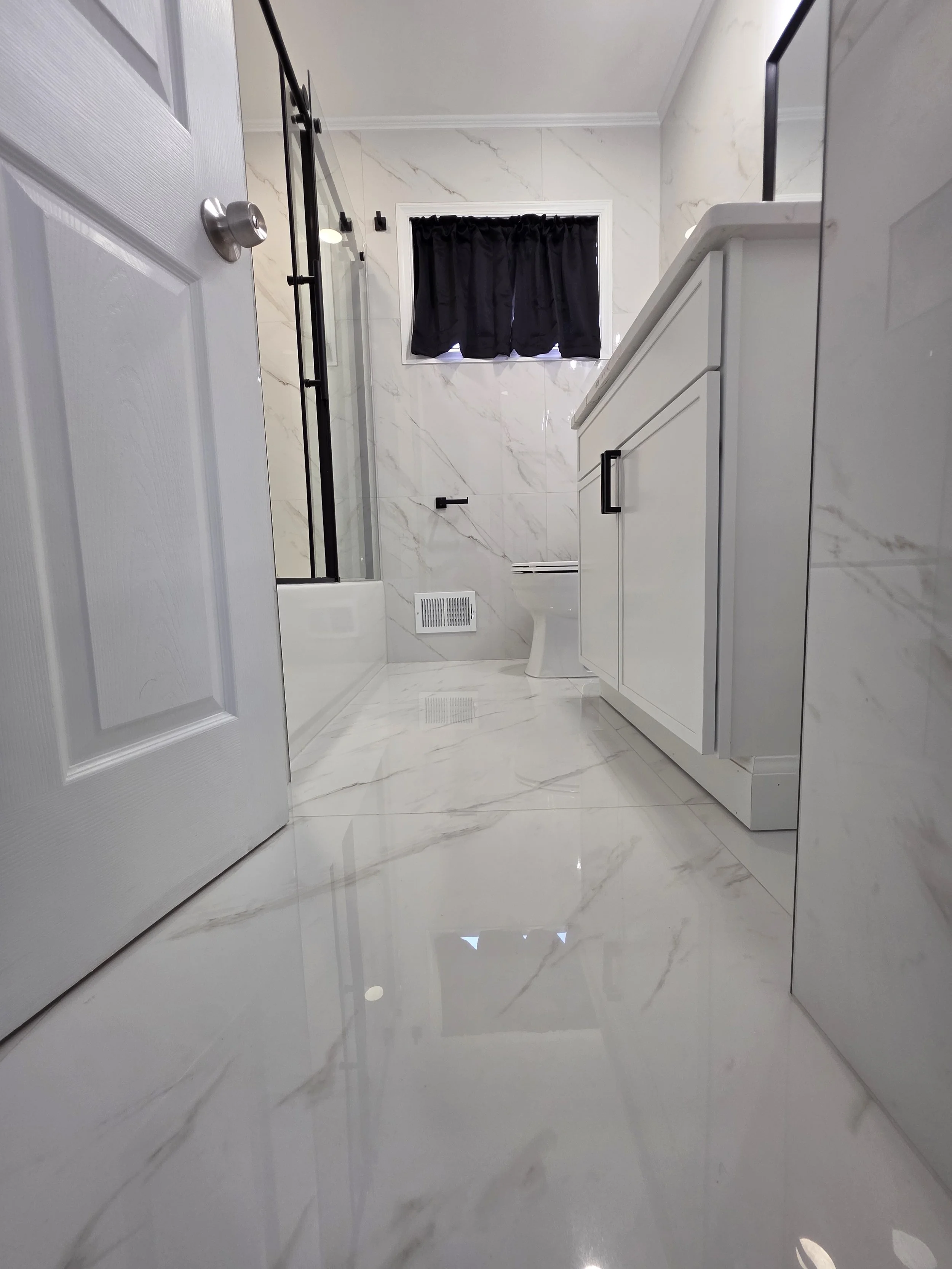 Low view across the marble-look bathroom floor toward the gray vanity and window.