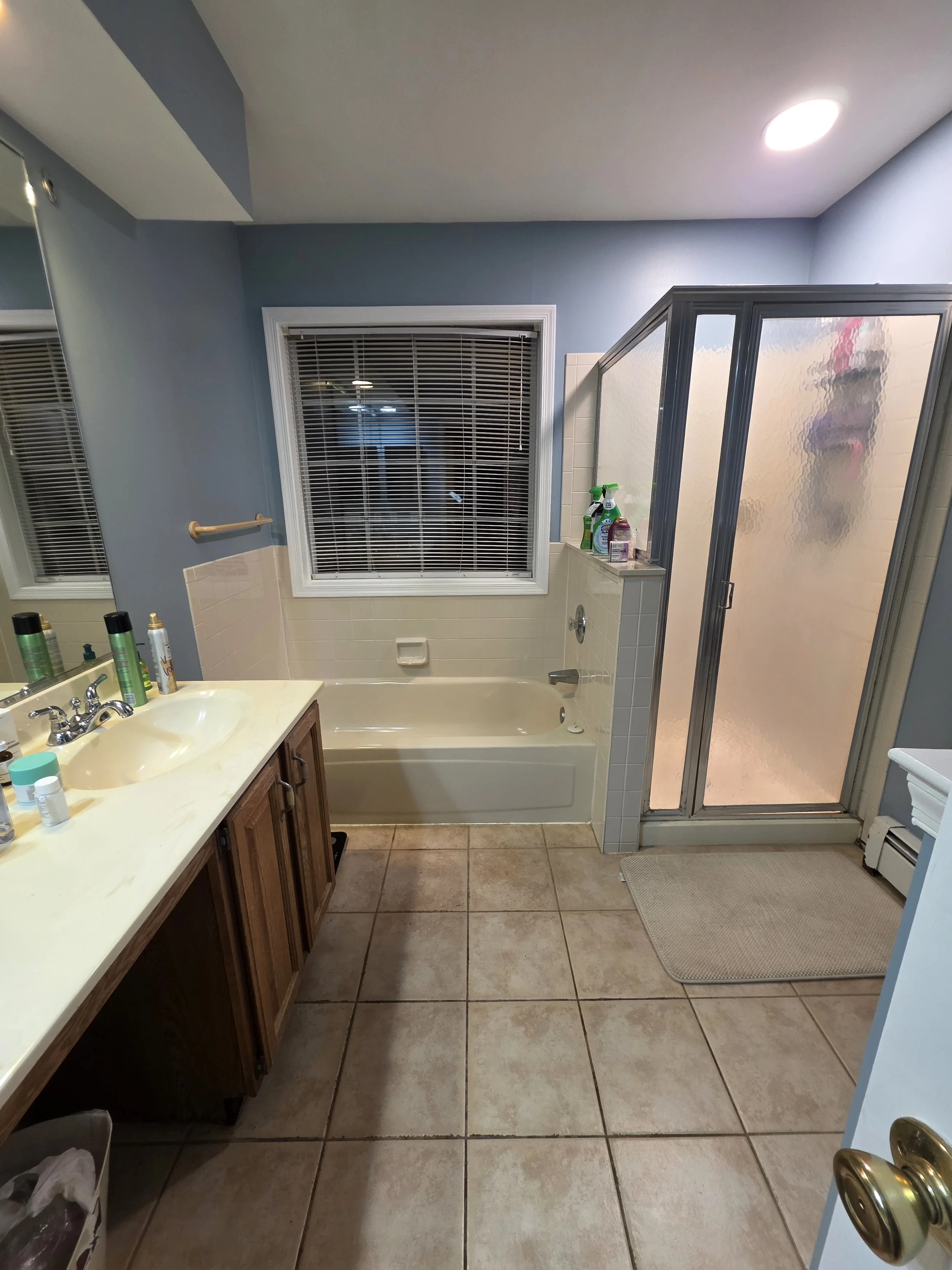 Before renovation: the original master bathroom with a built-in tub, framed shower and older vanity.