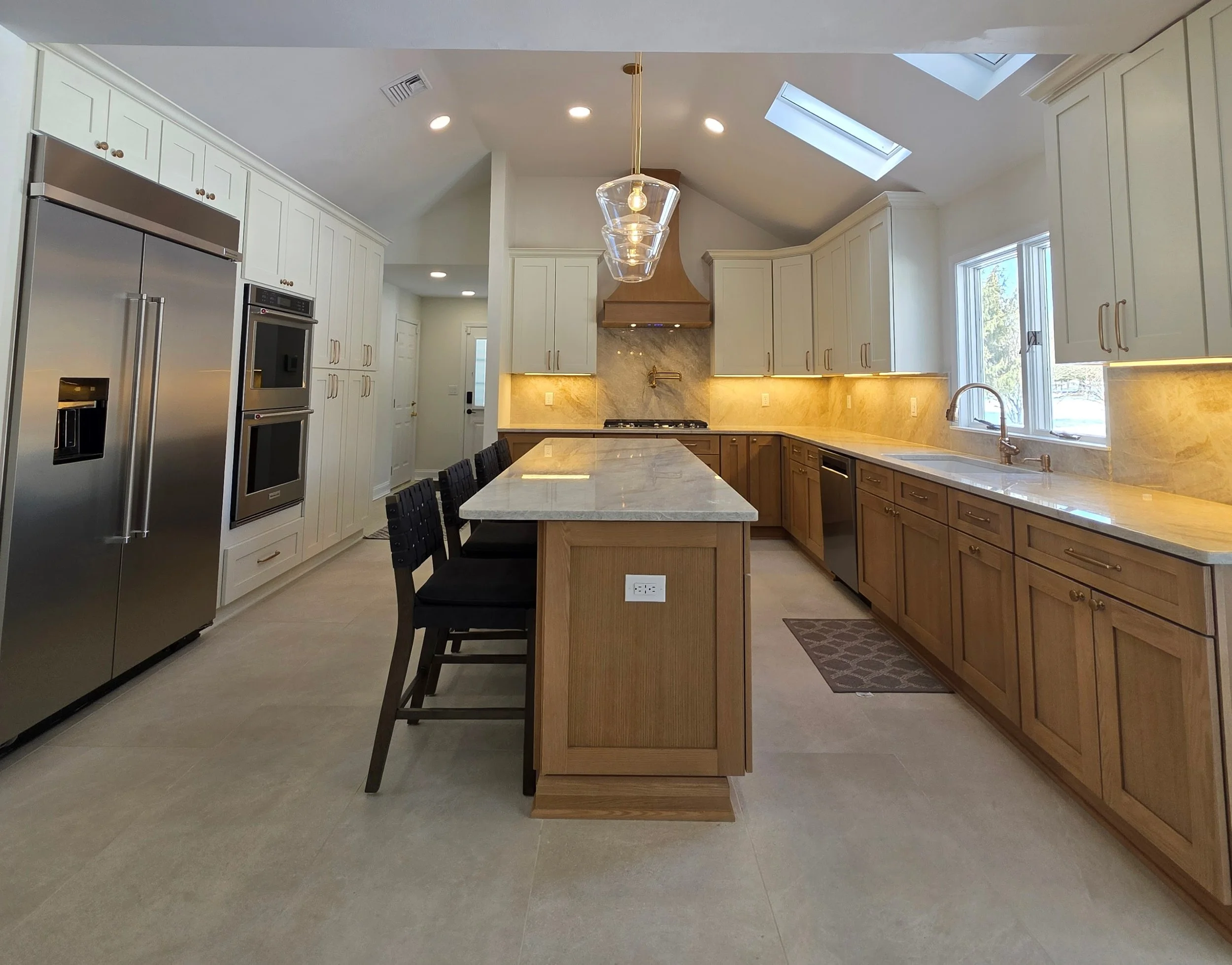 View down the island toward the custom wood range hood and illuminated backsplash.