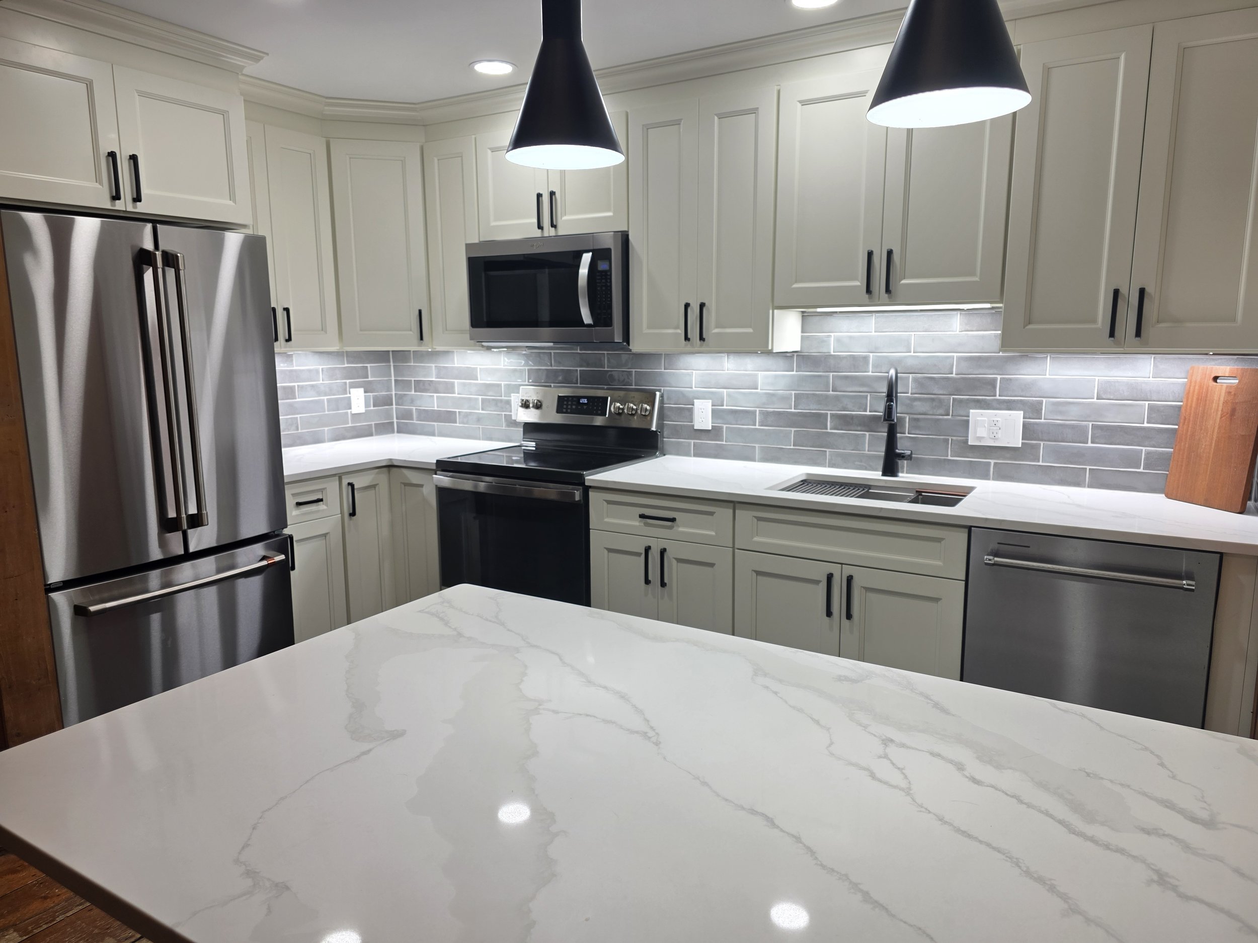 Donna and Chris’s remodeled kitchen with light cabinets, a veined peninsula and dark pendant lights.
