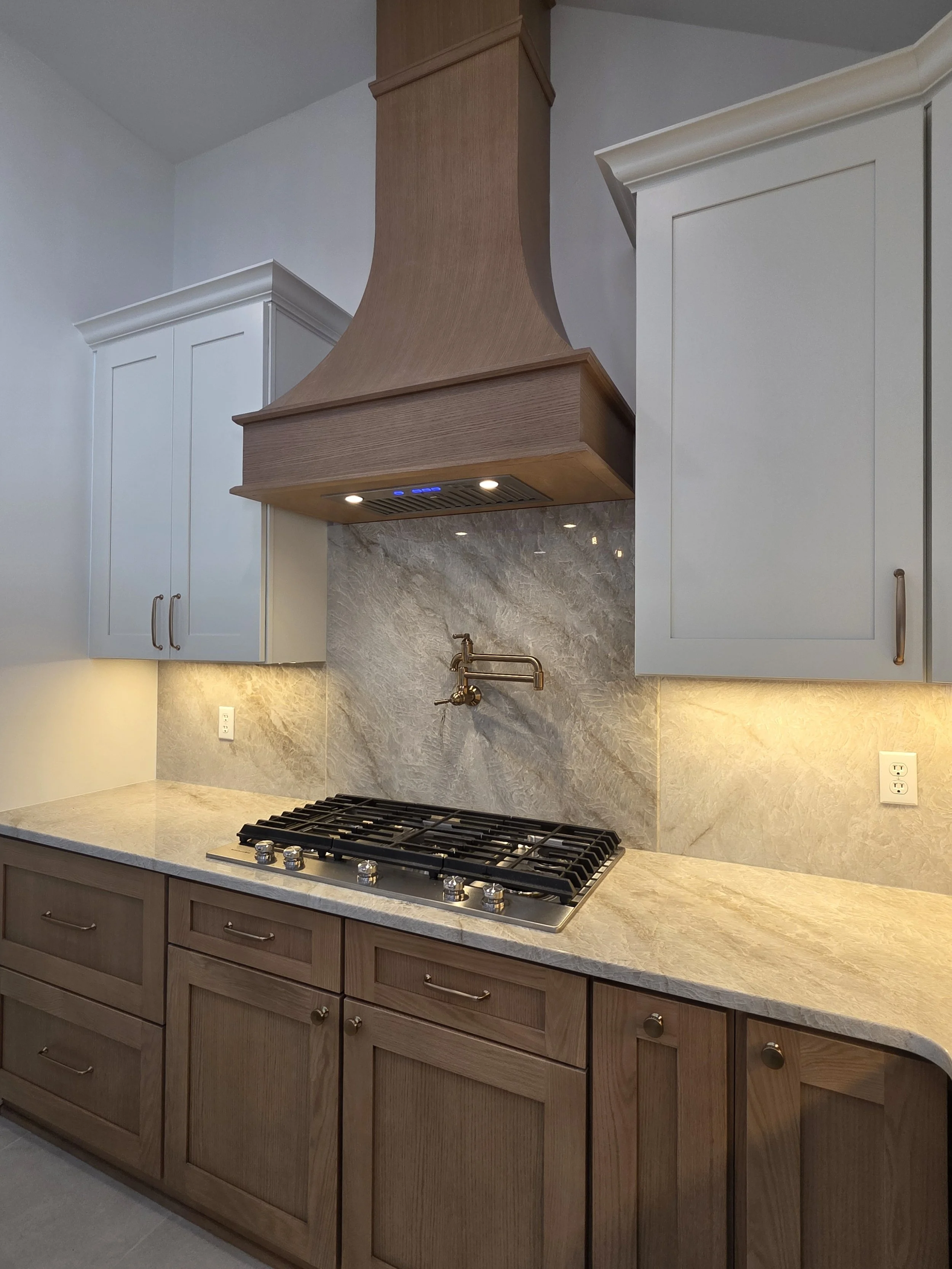 Custom wood range hood and cooktop against a veined backsplash with a gold-tone pot filler.