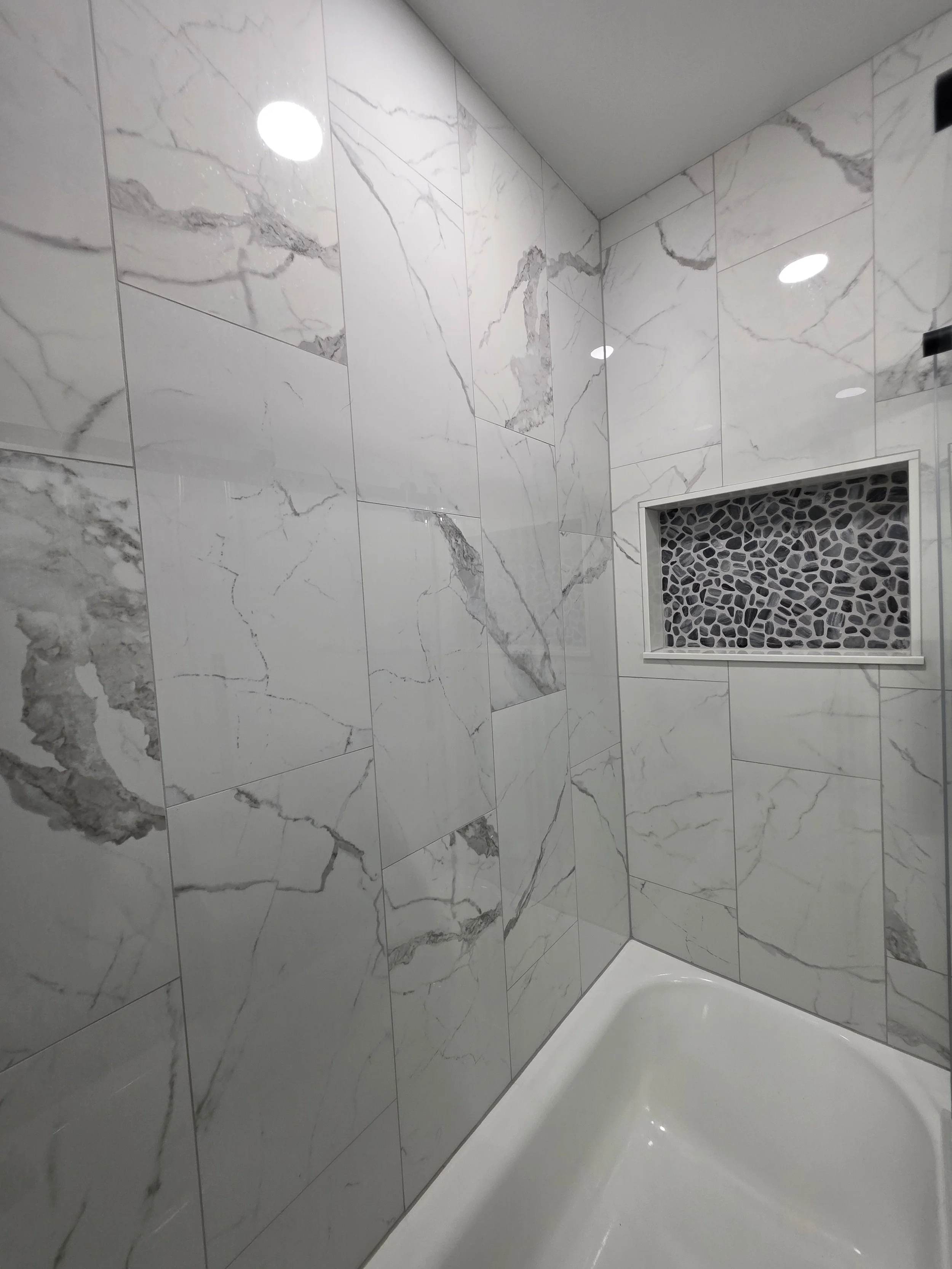 Angled view of the white bathtub and tiled walls with a pebble-pattern recessed niche.