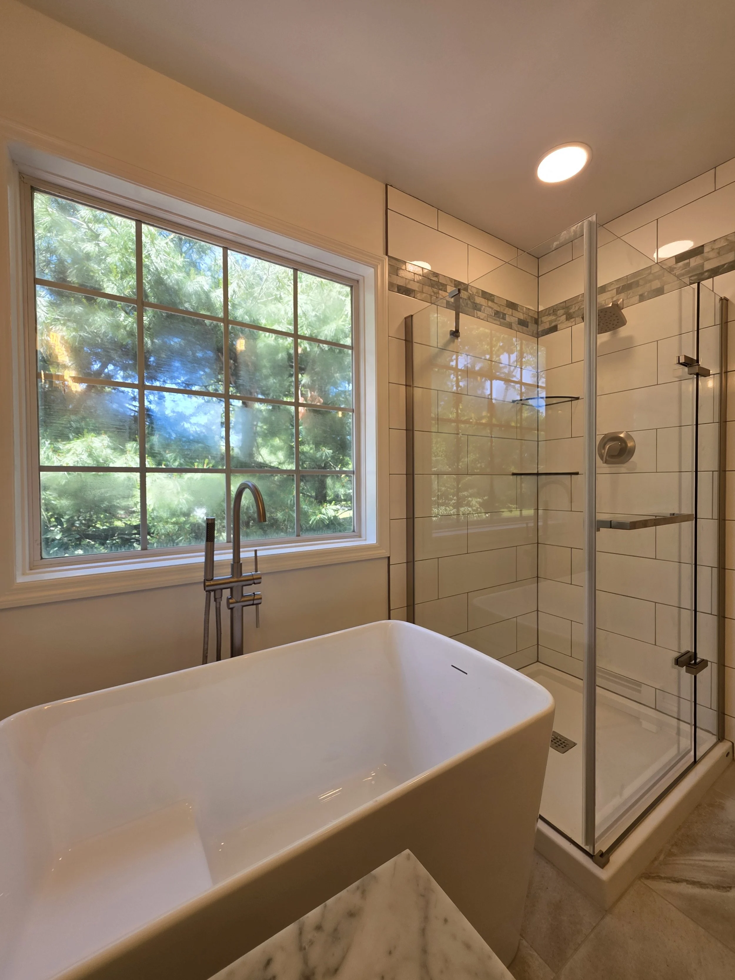 Freestanding bathtub beneath the large window, beside a glass shower enclosure.