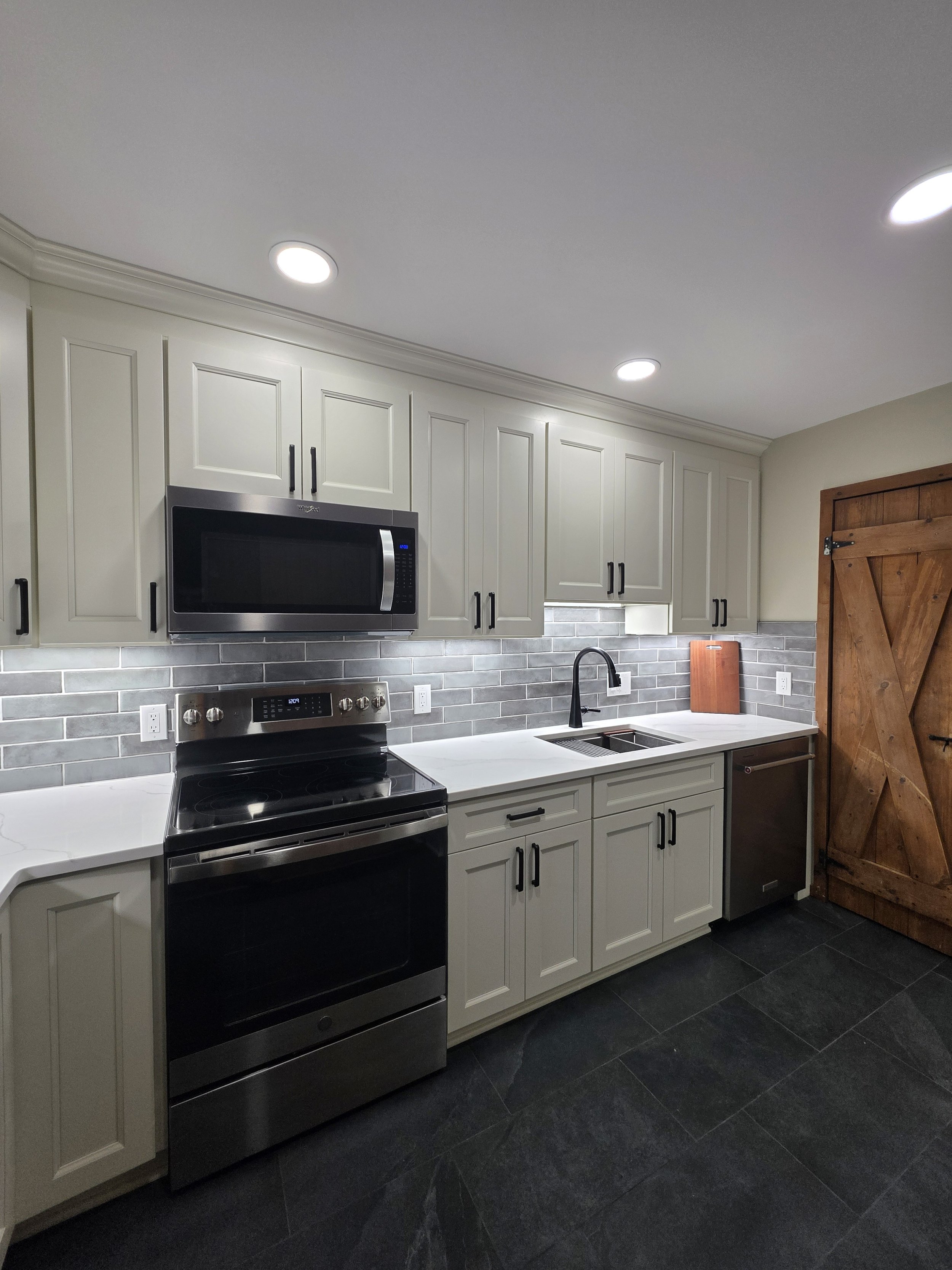 Range and sink wall with illuminated gray tile backsplash and dark cabinet hardware.