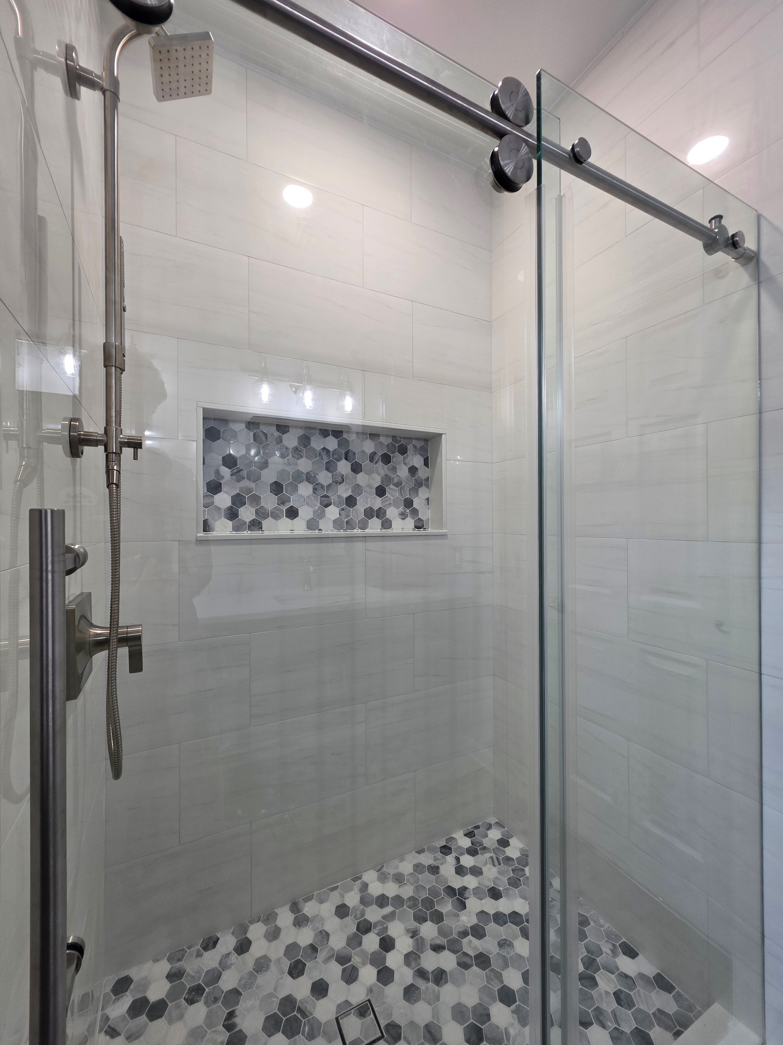 Glass shower enclosure with mosaic tile niche.