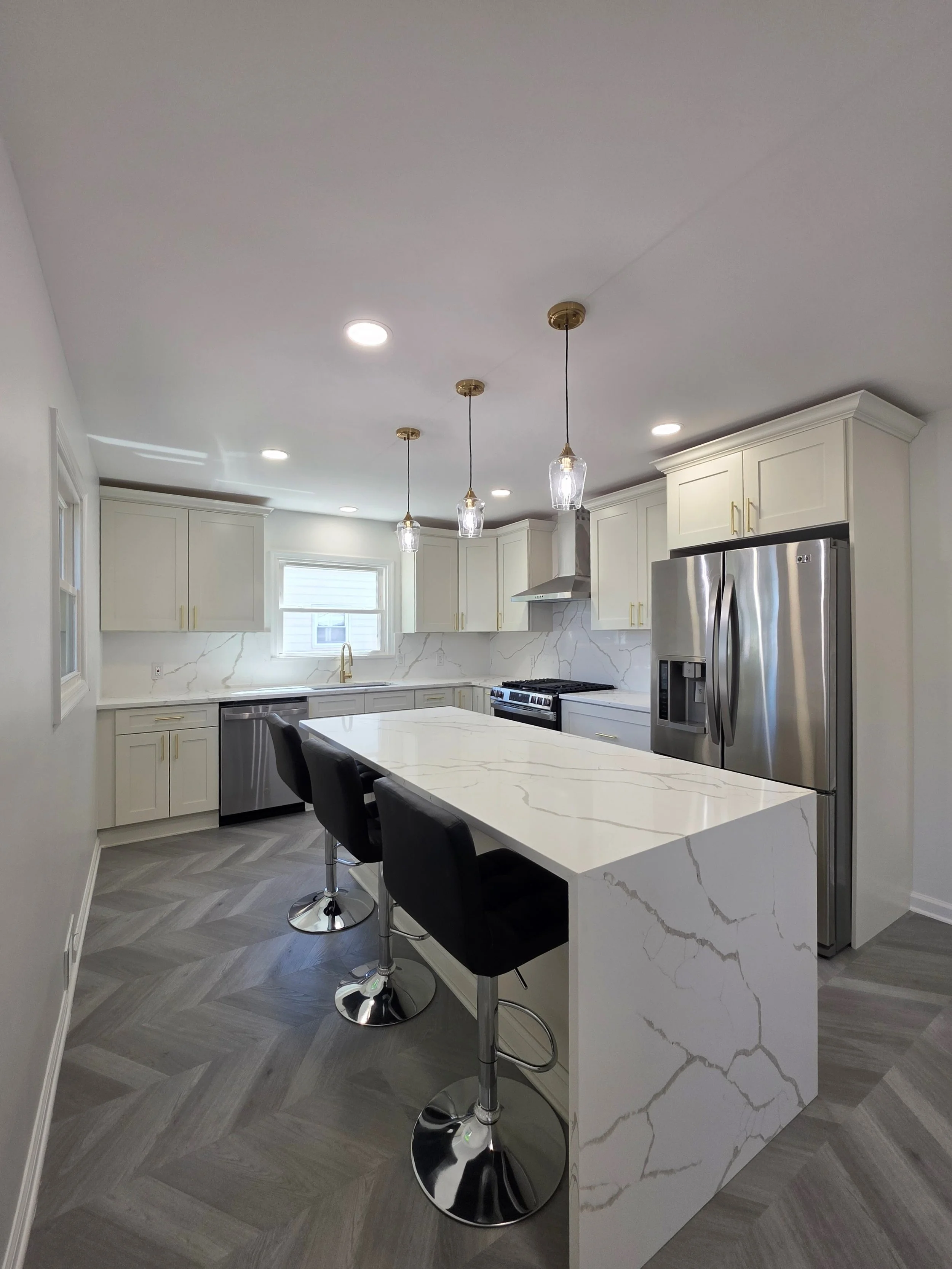 Samuel’s remodeled kitchen with a veined waterfall island, seating and pendant lights.