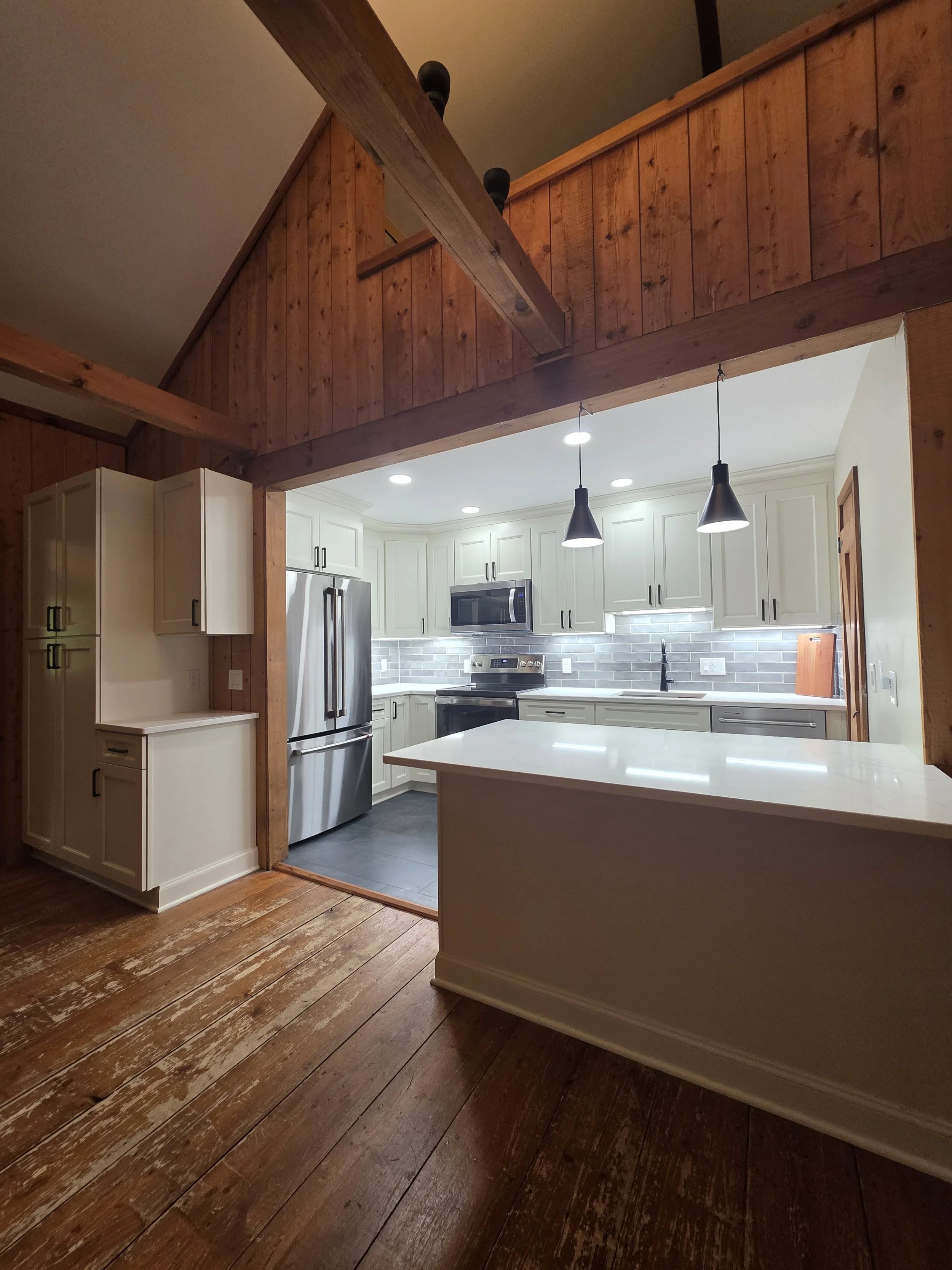 View into the remodeled kitchen beneath exposed wood beams from the adjoining room.