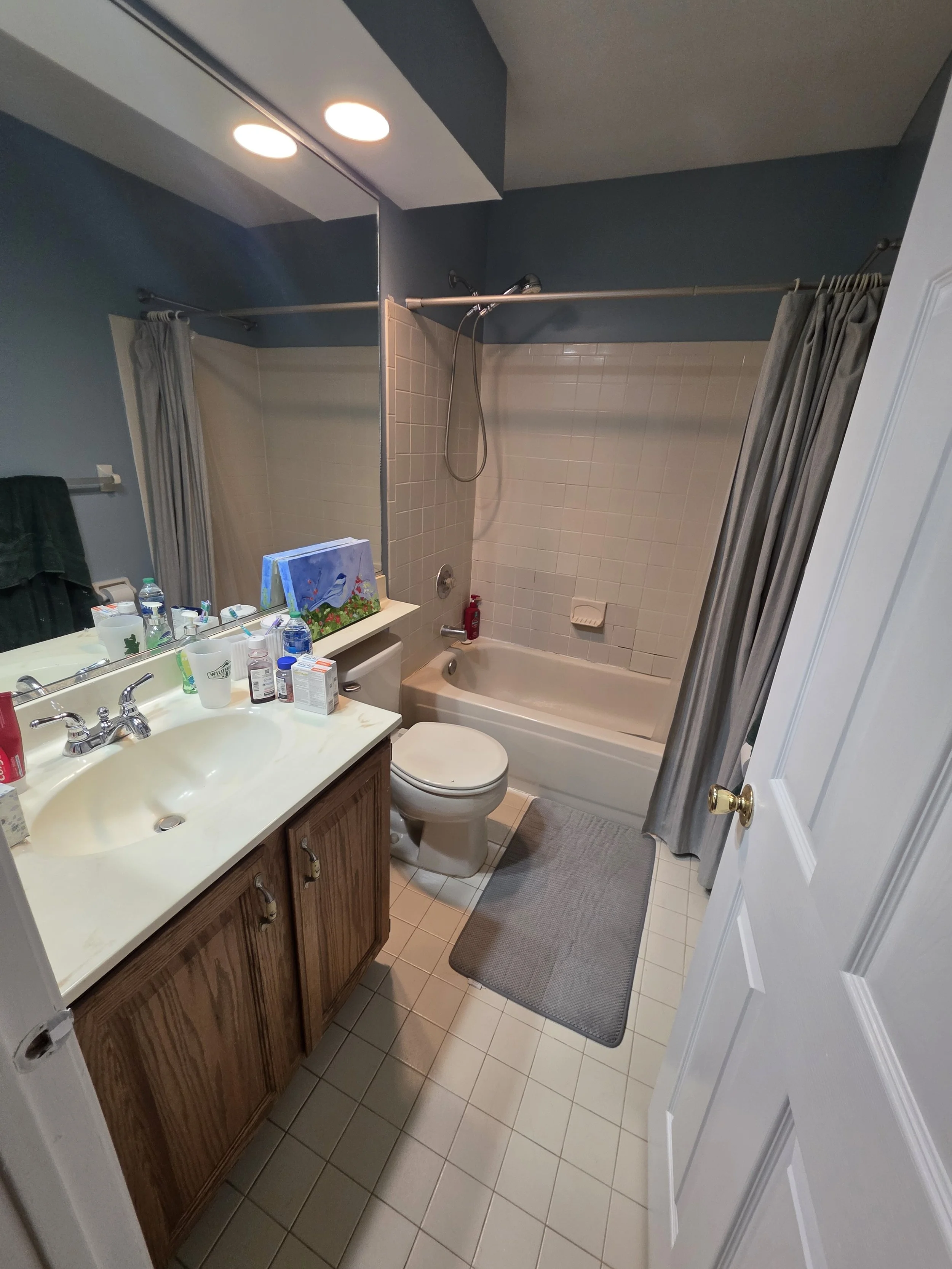 Before renovation: the original hallway bathroom with a wood vanity, blue walls and a shower curtain.