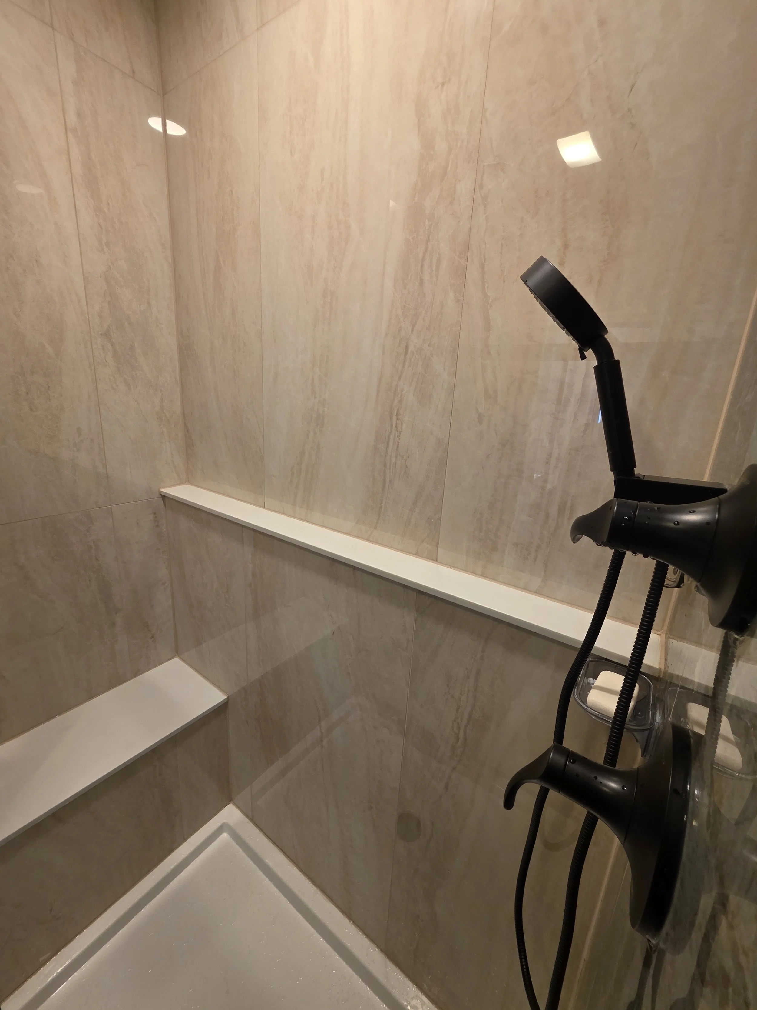 Shower wall detail with a long white ledge, small corner bench and handheld spray.