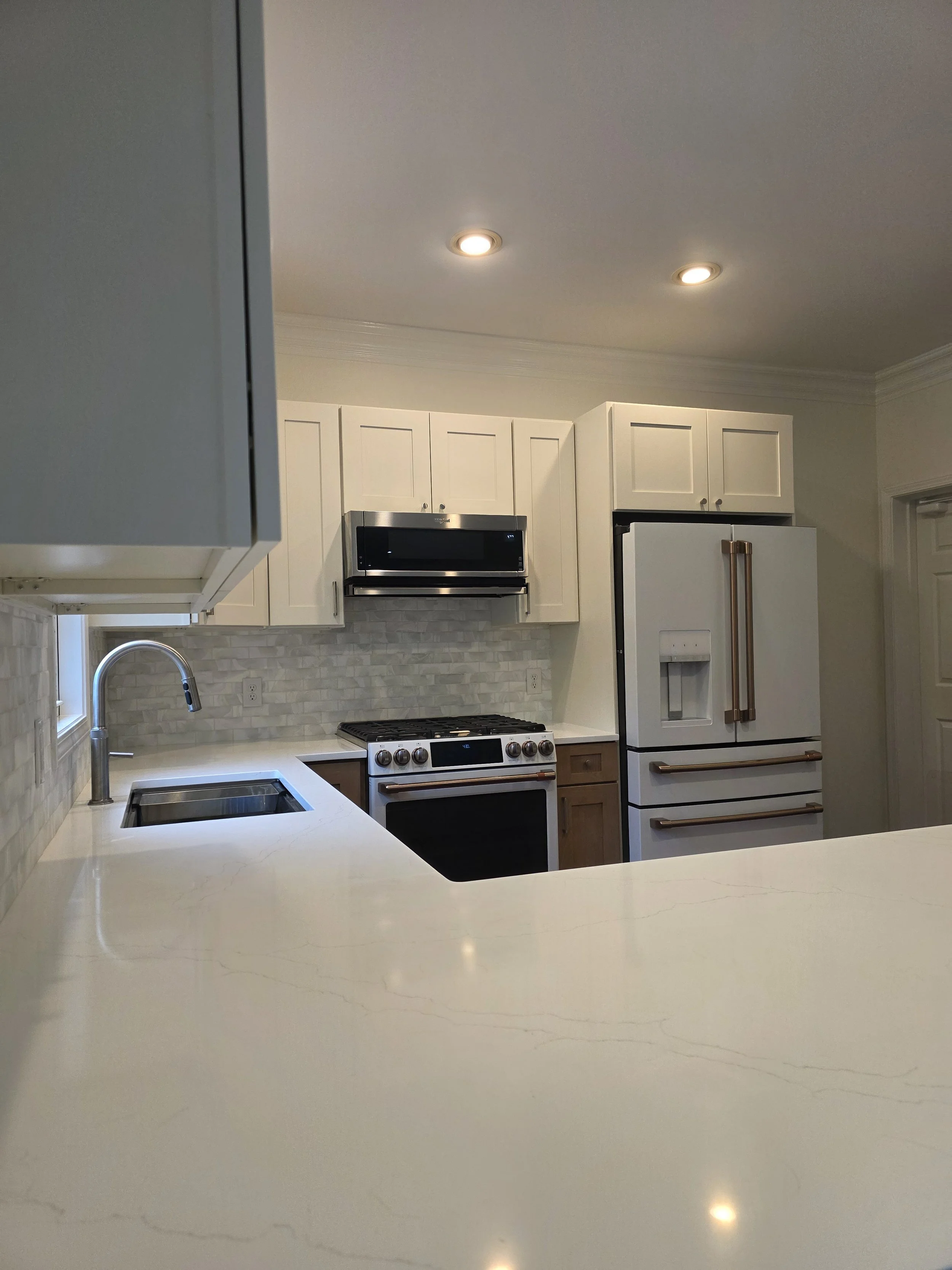 Kitchen sink and cooking area with light countertops, a tile backsplash, and two-tone cabinets.