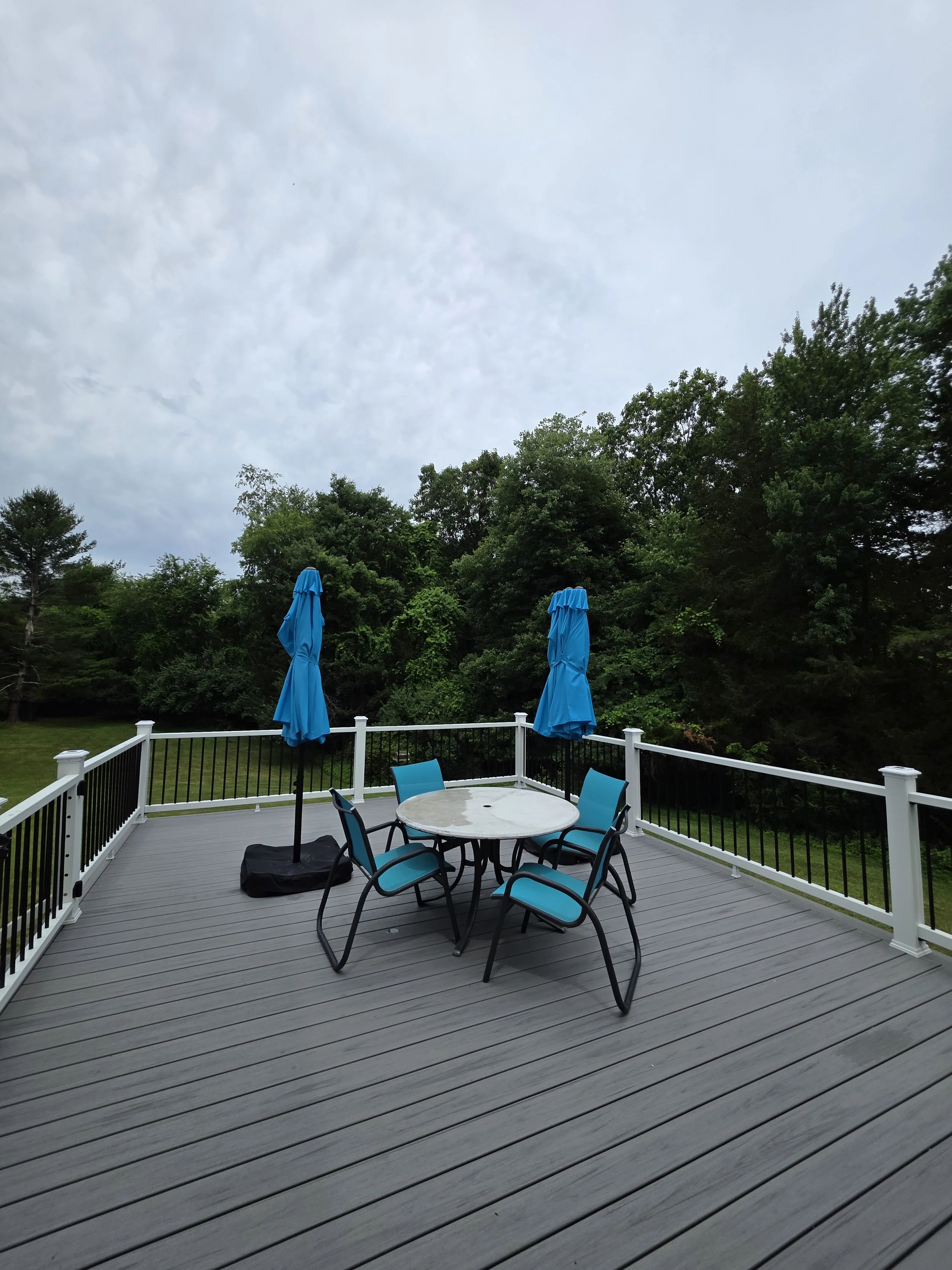 Gray deck surface overlooking the backyard, with an outdoor dining table and blue umbrellas.