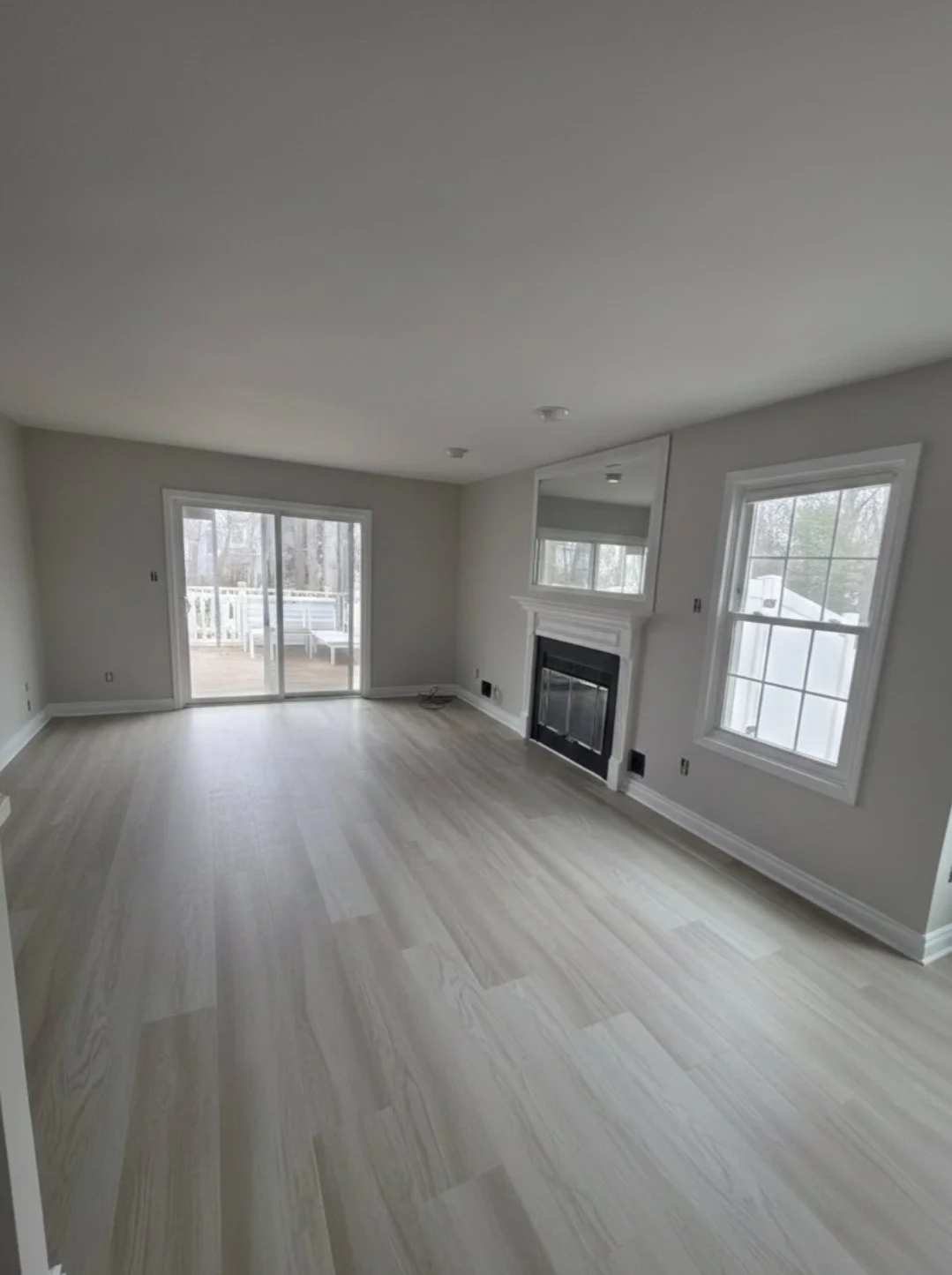 Refinished living room floor beside the fireplace, windows and sliding door.