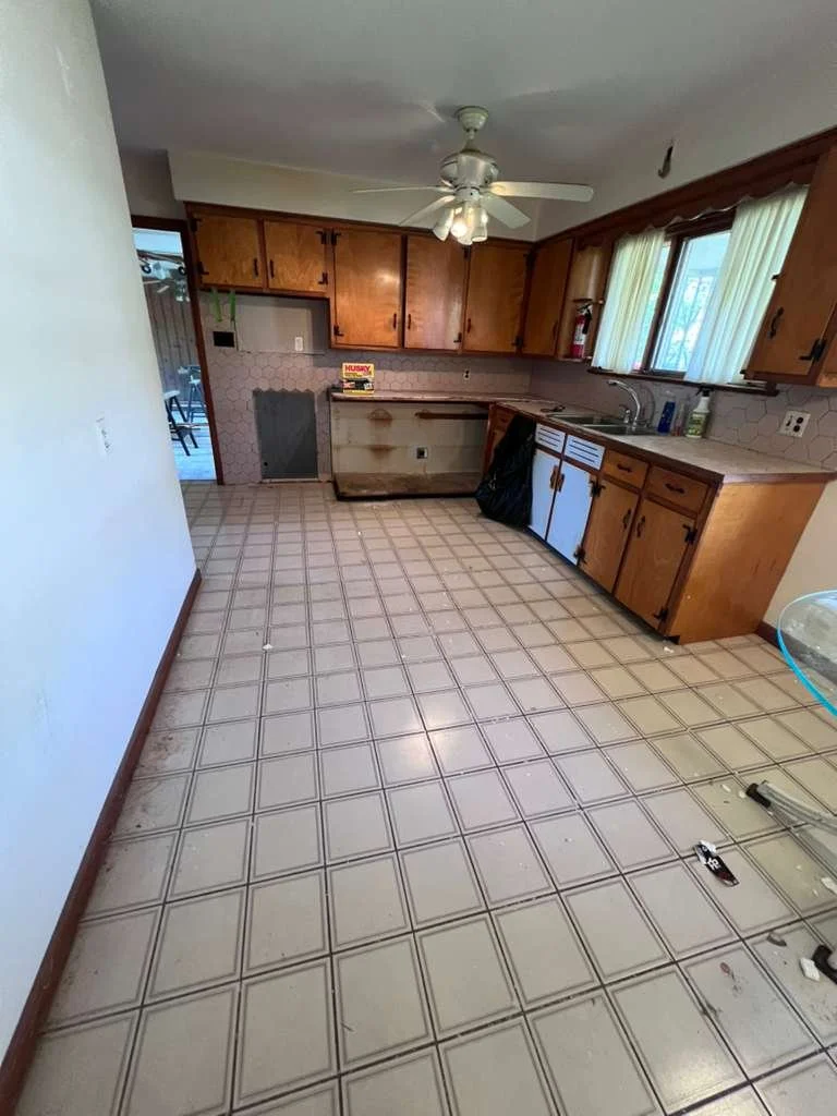 Kitchen before renovation with wood cabinetry and older tile floor.