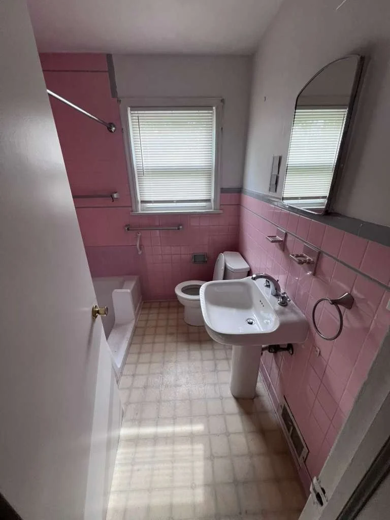 Before renovation: the original hallway bathroom with pink wall tile, pedestal sink and older tub area.