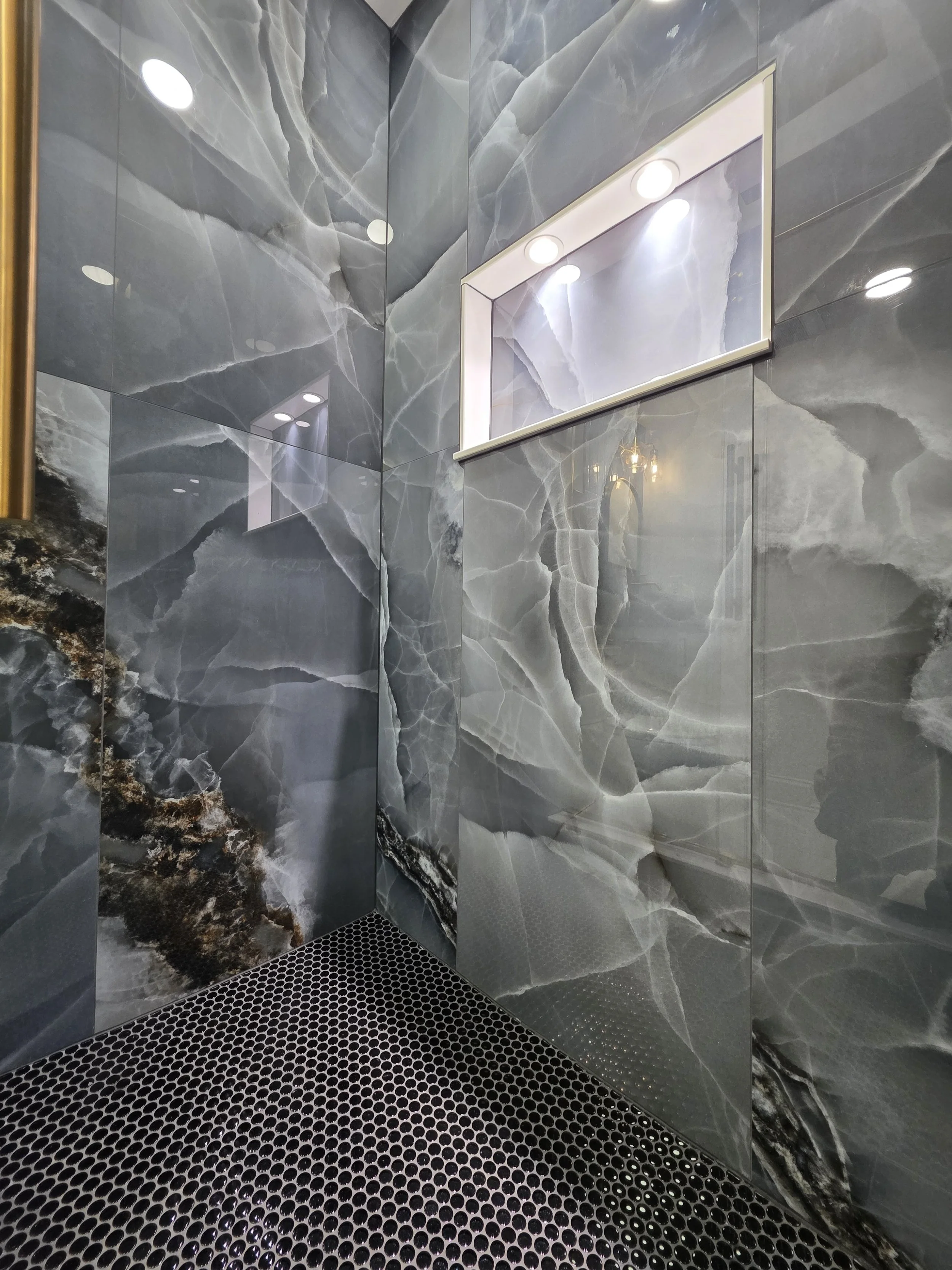 Veined shower walls above a dark mosaic floor, with an illuminated recessed niche.