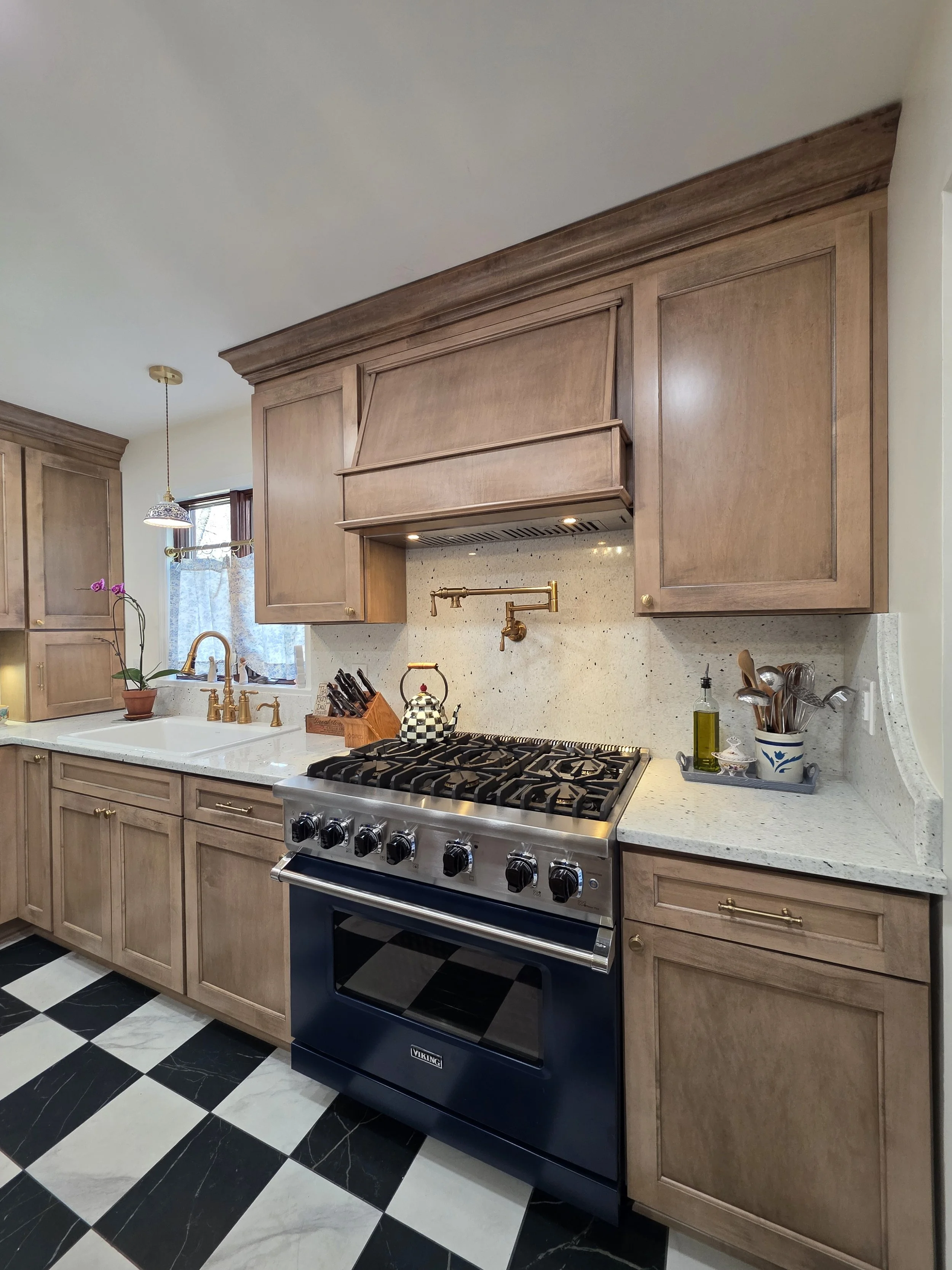 Wood range hood and dark range framed by matching cabinetry and a light backsplash.