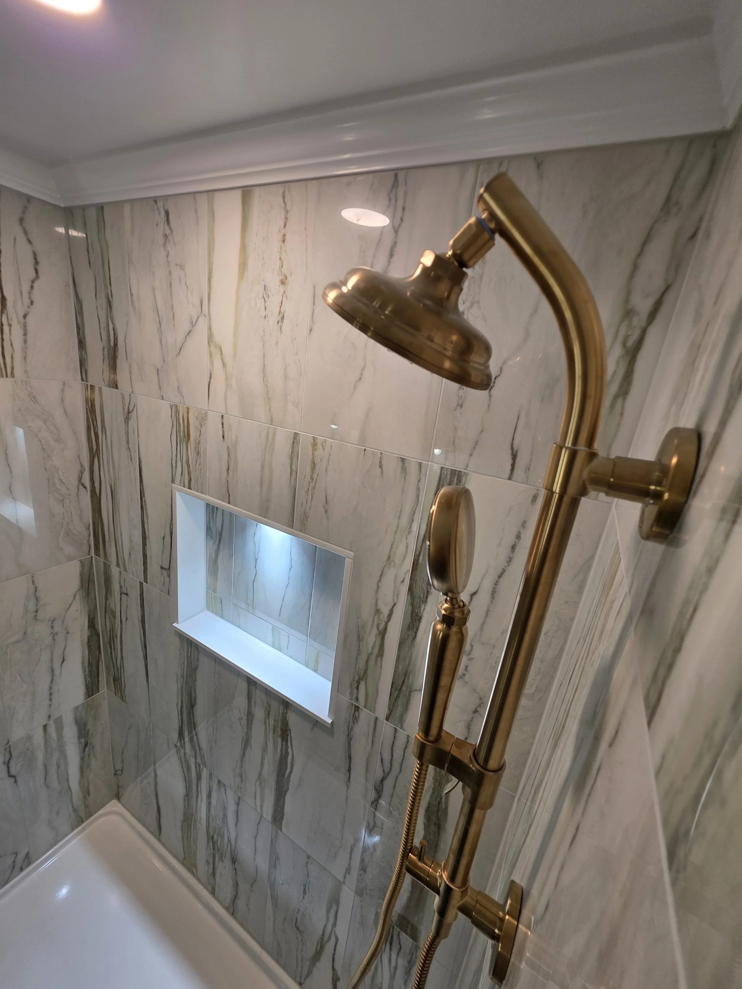 Gold-toned shower fixtures against veined wall tile.